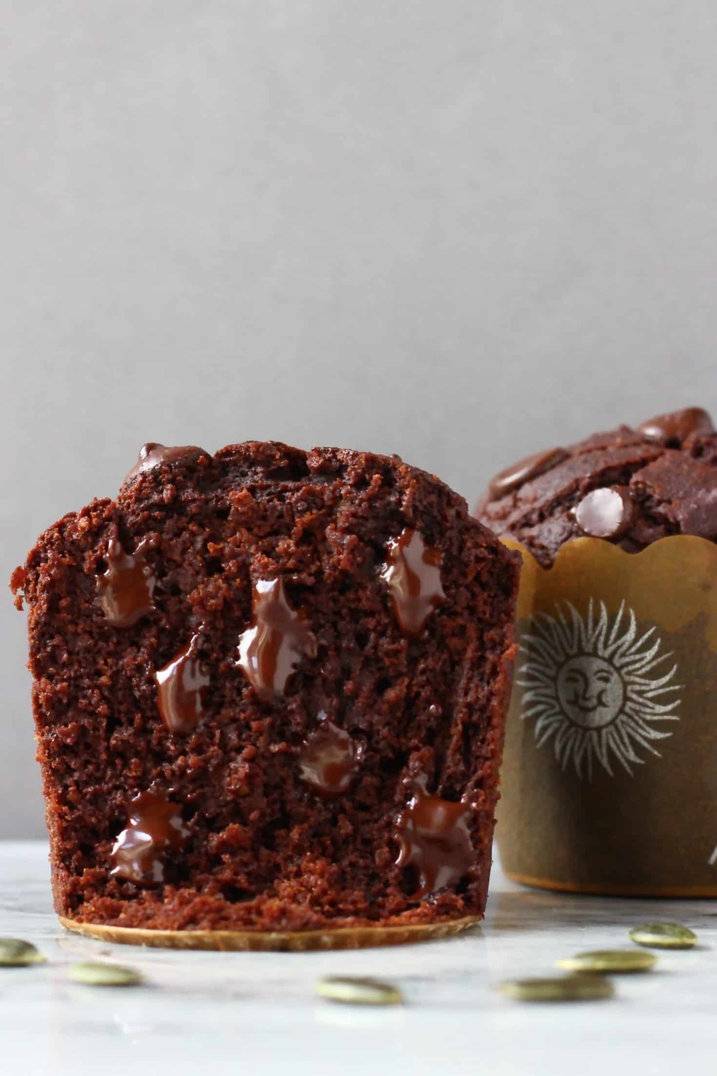 A halved gluten-free vegan chocolate pumpkin muffin on a marble slab with pumpkin seeds