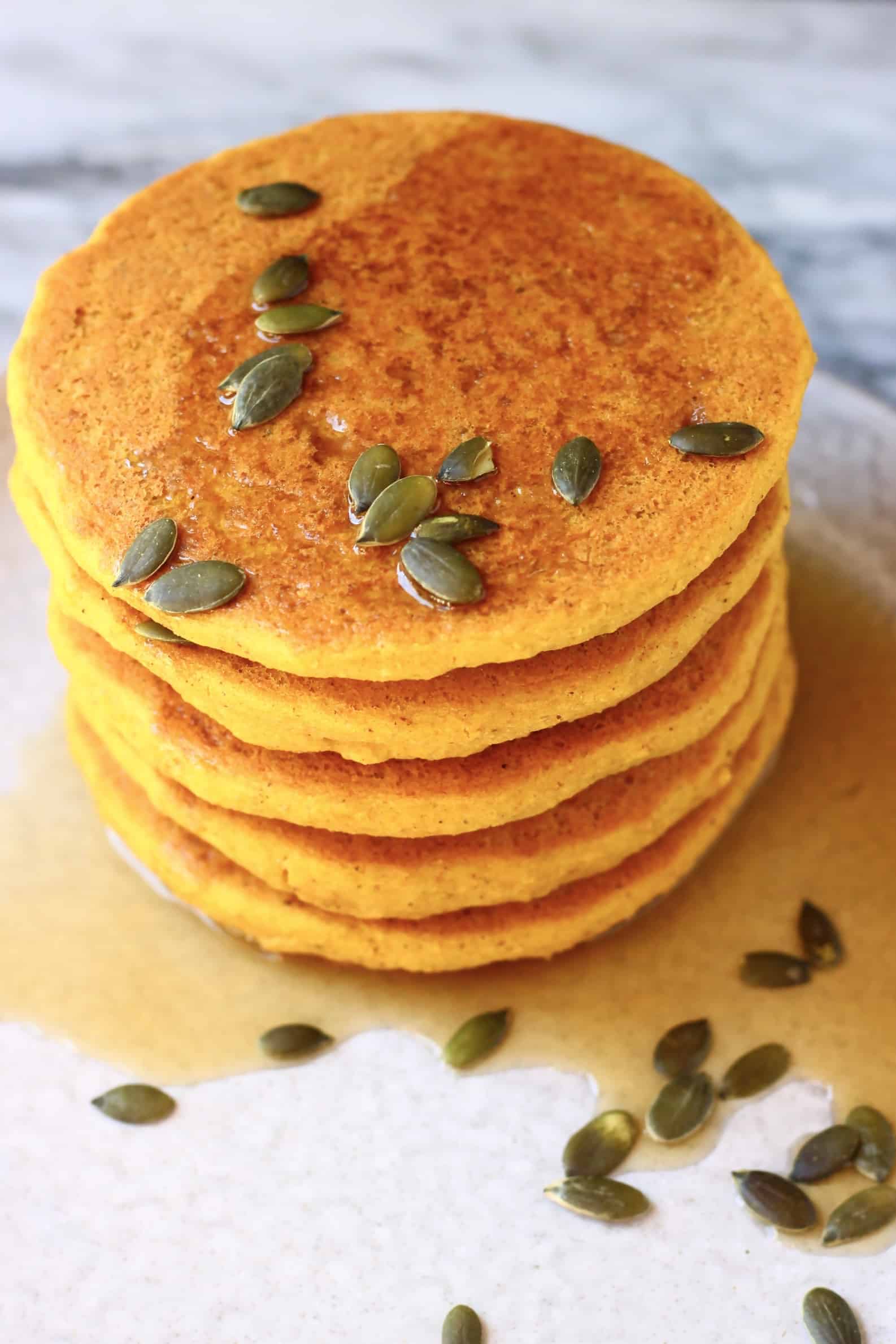A stack of gluten-free vegan pancakes on a plate topped with syrup and pumpkin seeds