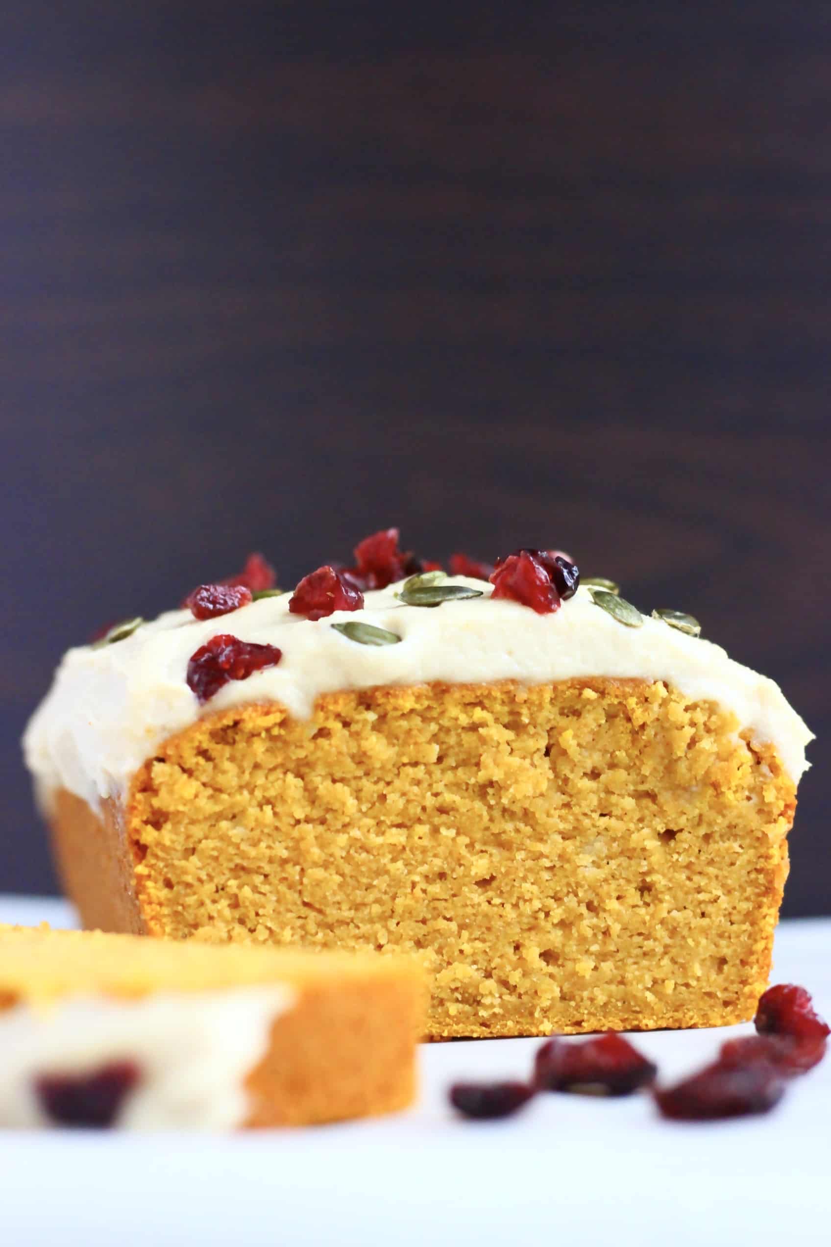 A sliced gluten-free vegan pumpkin loaf cake topped with cream cheese frosting, dried cranberries and pumpkin seeds