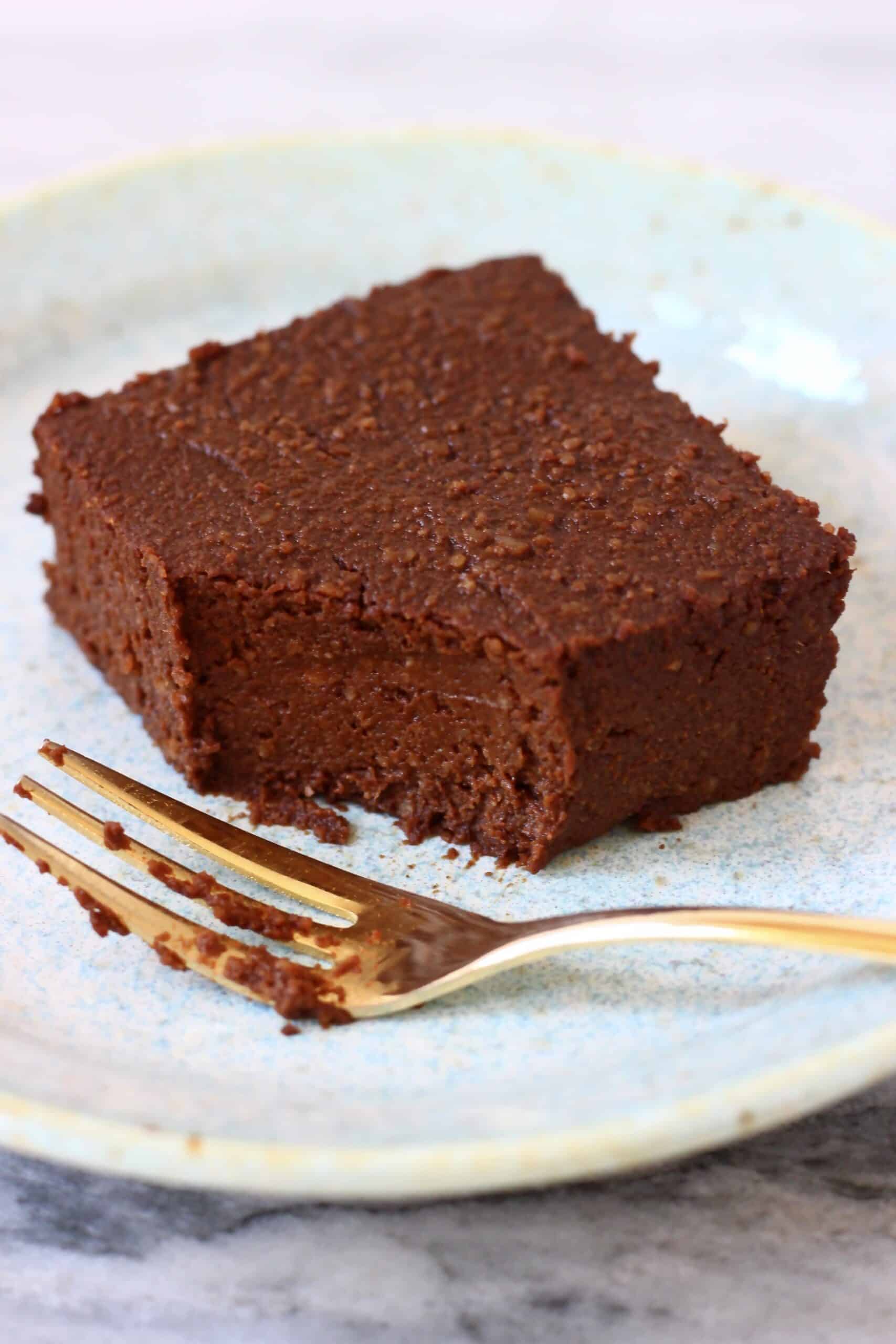 A pumpkin brownie with a mouthful taken out of it on a light blue plate with a gold fork