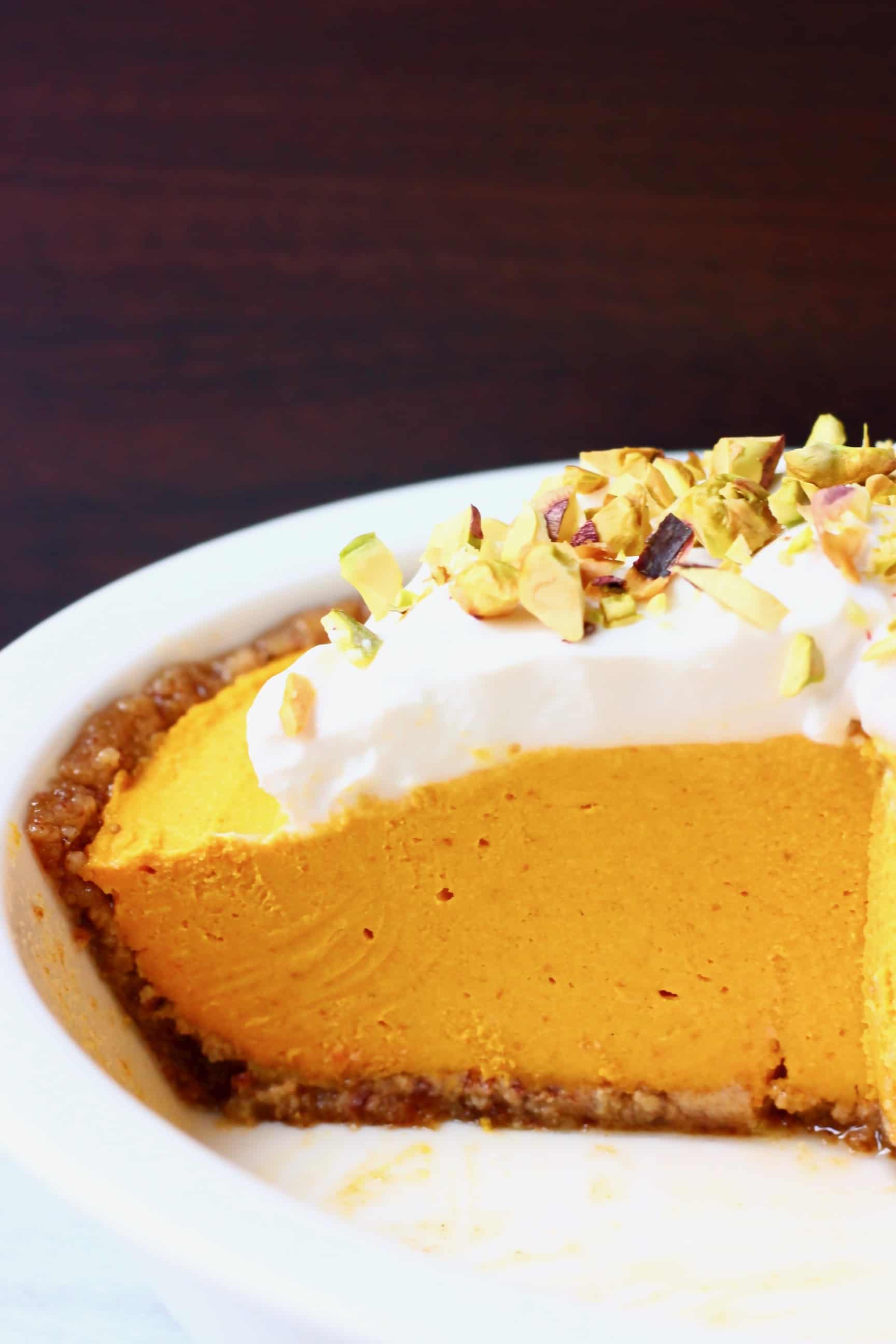 A white pie dish with no-bake pumpkin pie topped with whipped cream and chopped pistachios against a dark brown background