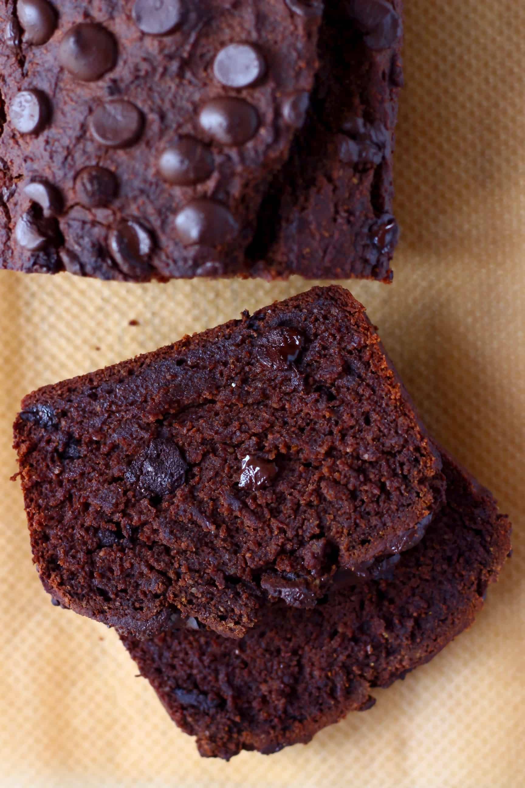 A loaf of chocolate pumpkin bread with two slices next to it against a sheet of brown baking paper