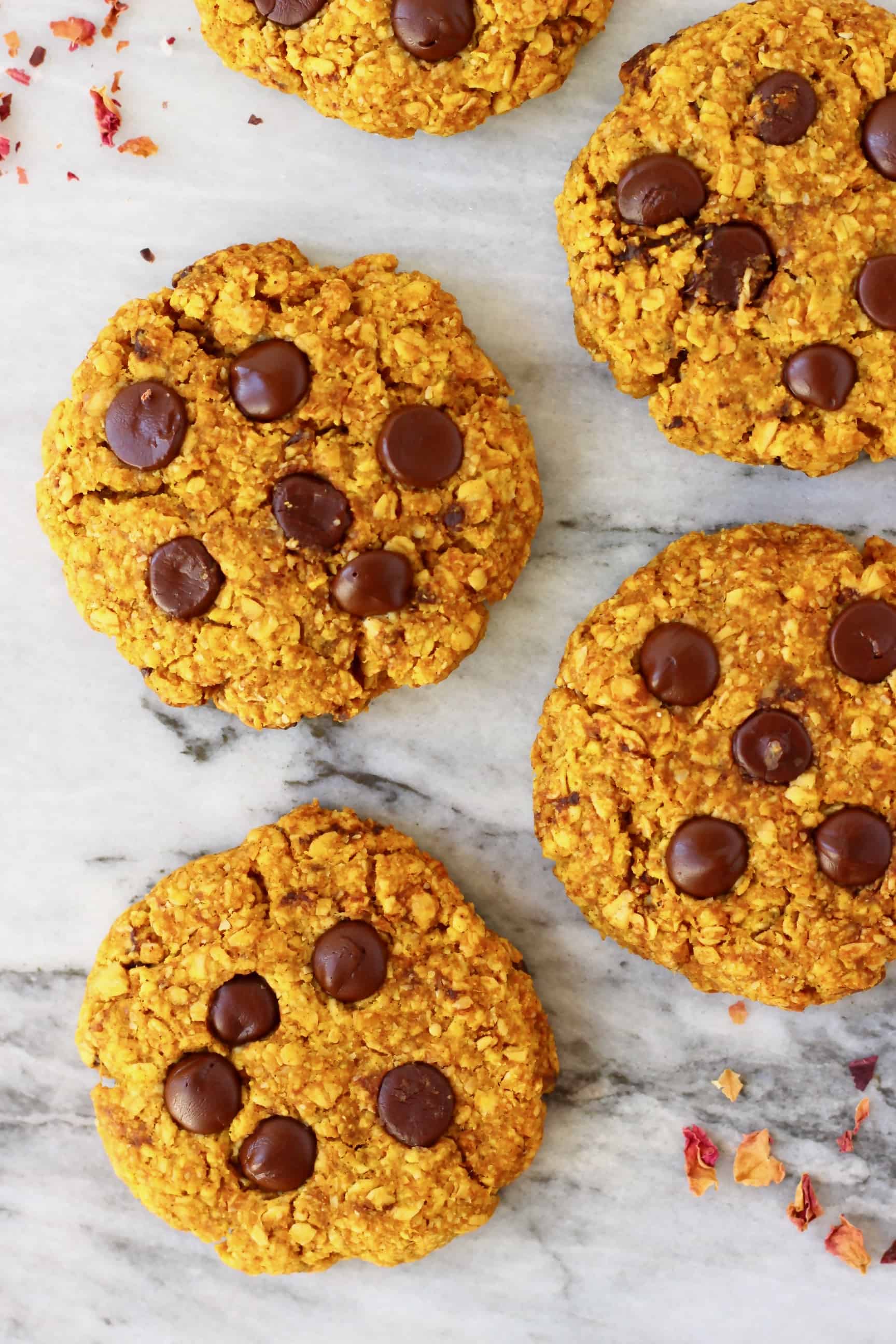 Five pumpkin cookies with chocolate chips against a marble background