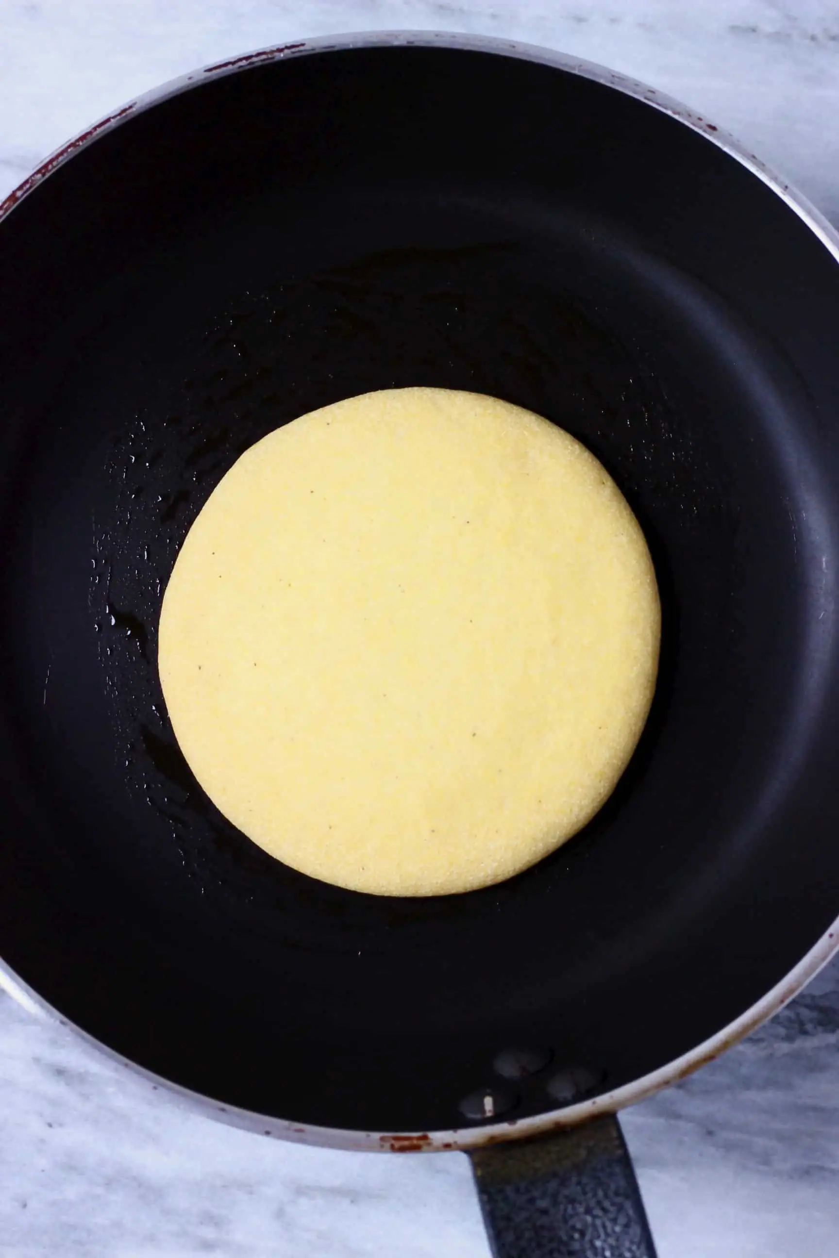 A raw gluten-free vegan cornmeal pancake in a frying pan 
