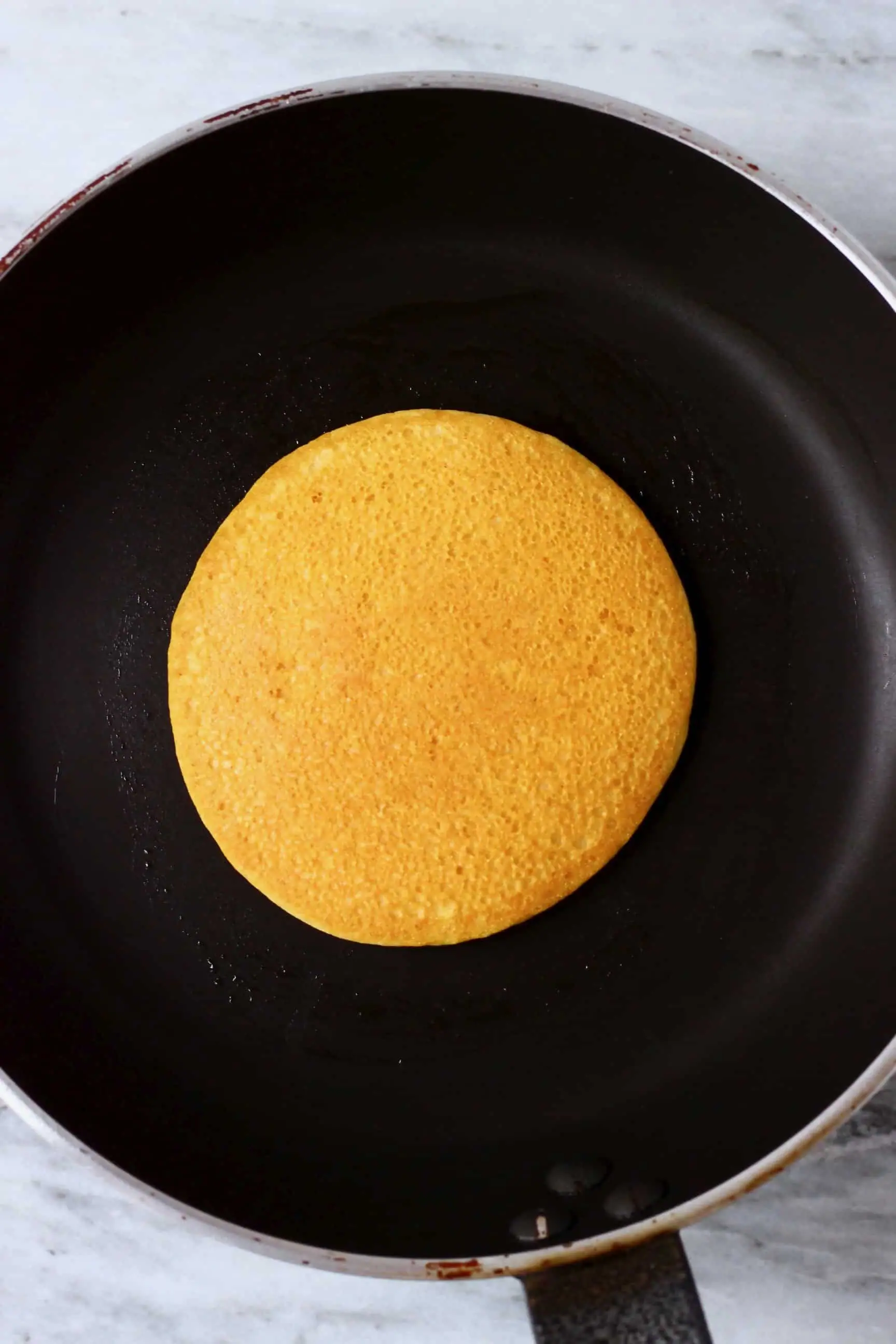 A golden brown gluten-free vegan cornmeal pancake in a frying pan
