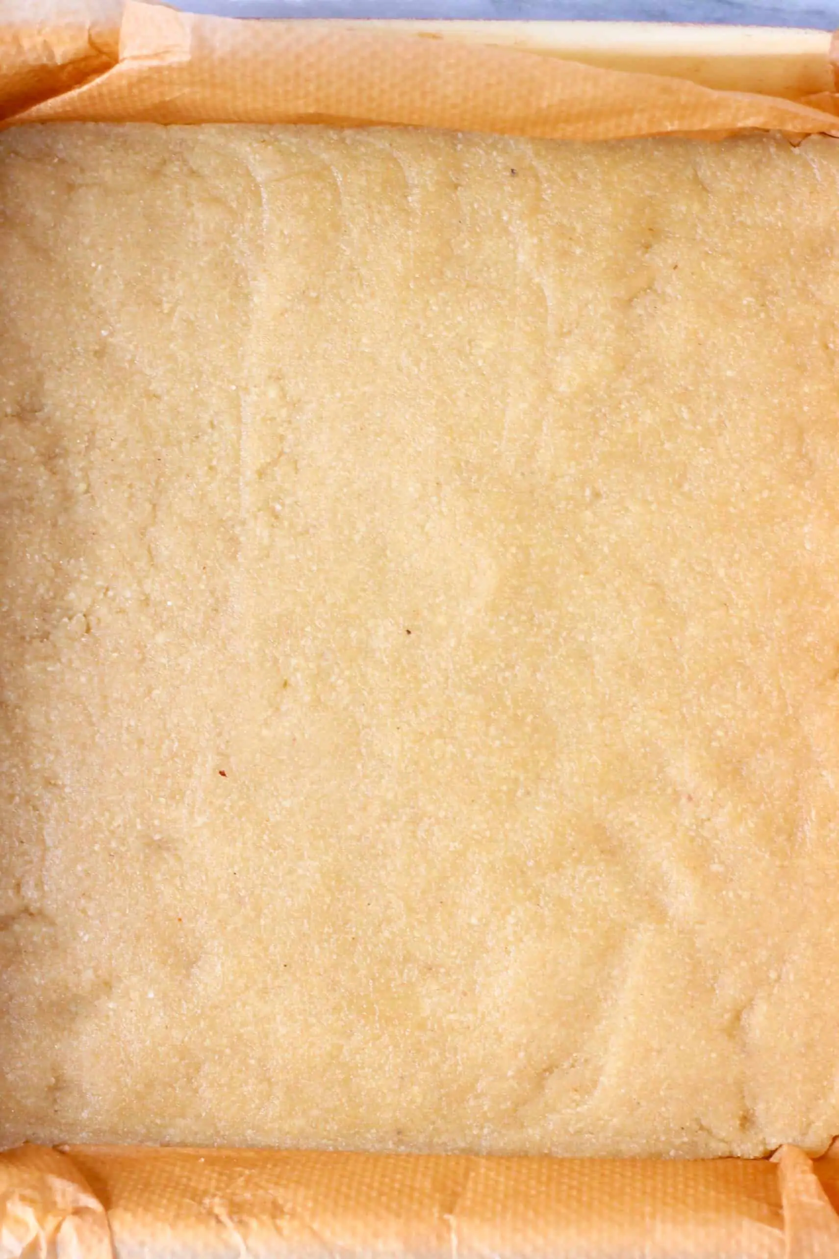 Raw gluten-free vegan shortbread cookie dough in a square baking tin lined with baking paper