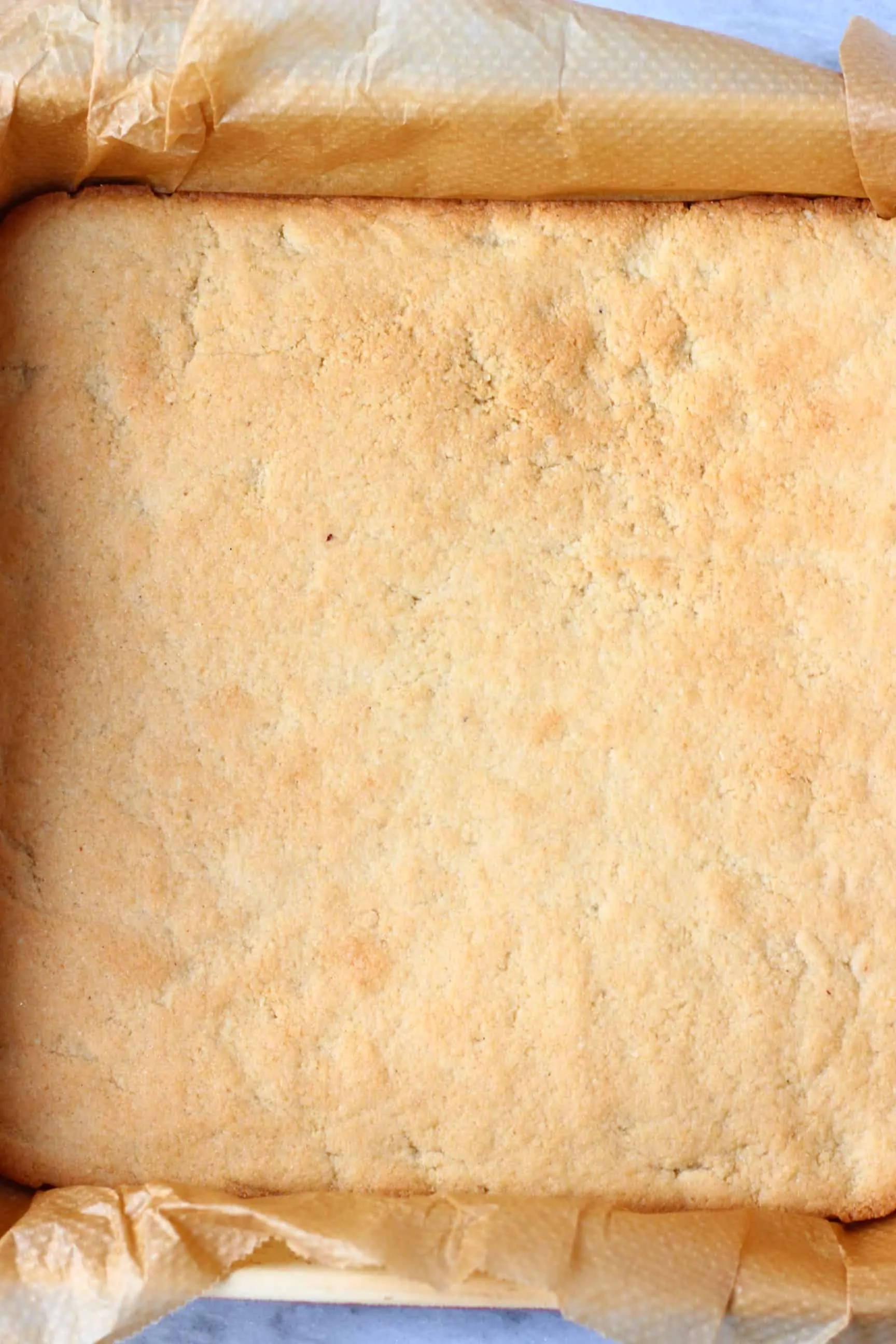 Baked gluten-free vegan shortbread cookie base in a square baking tin lined with baking paper