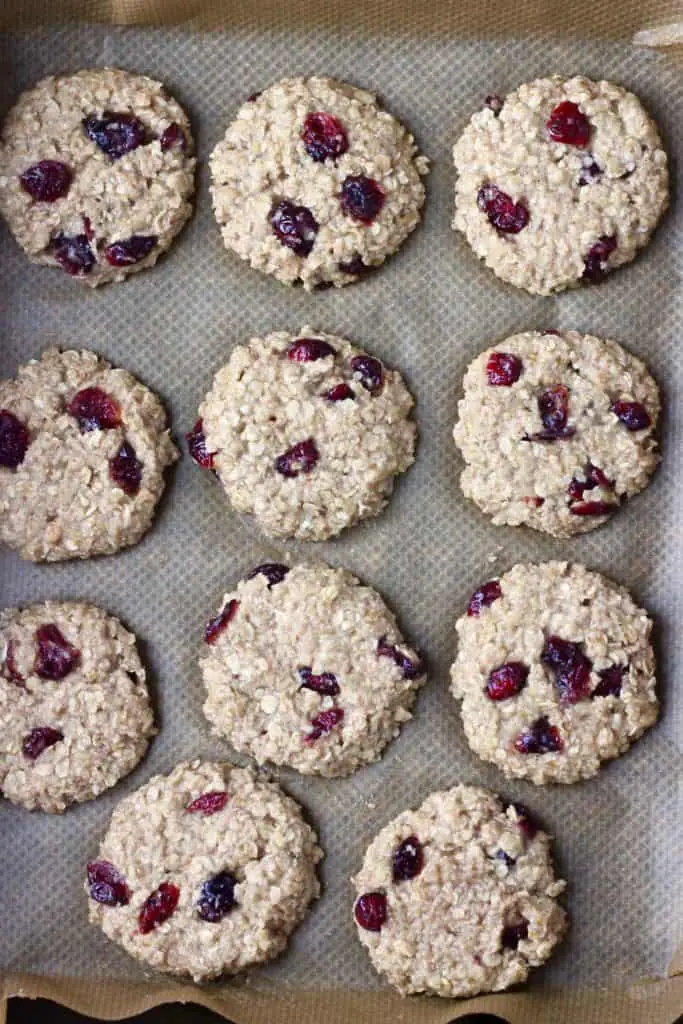 11 raw oatmeal cookies with dried cranberries on brown baking paper