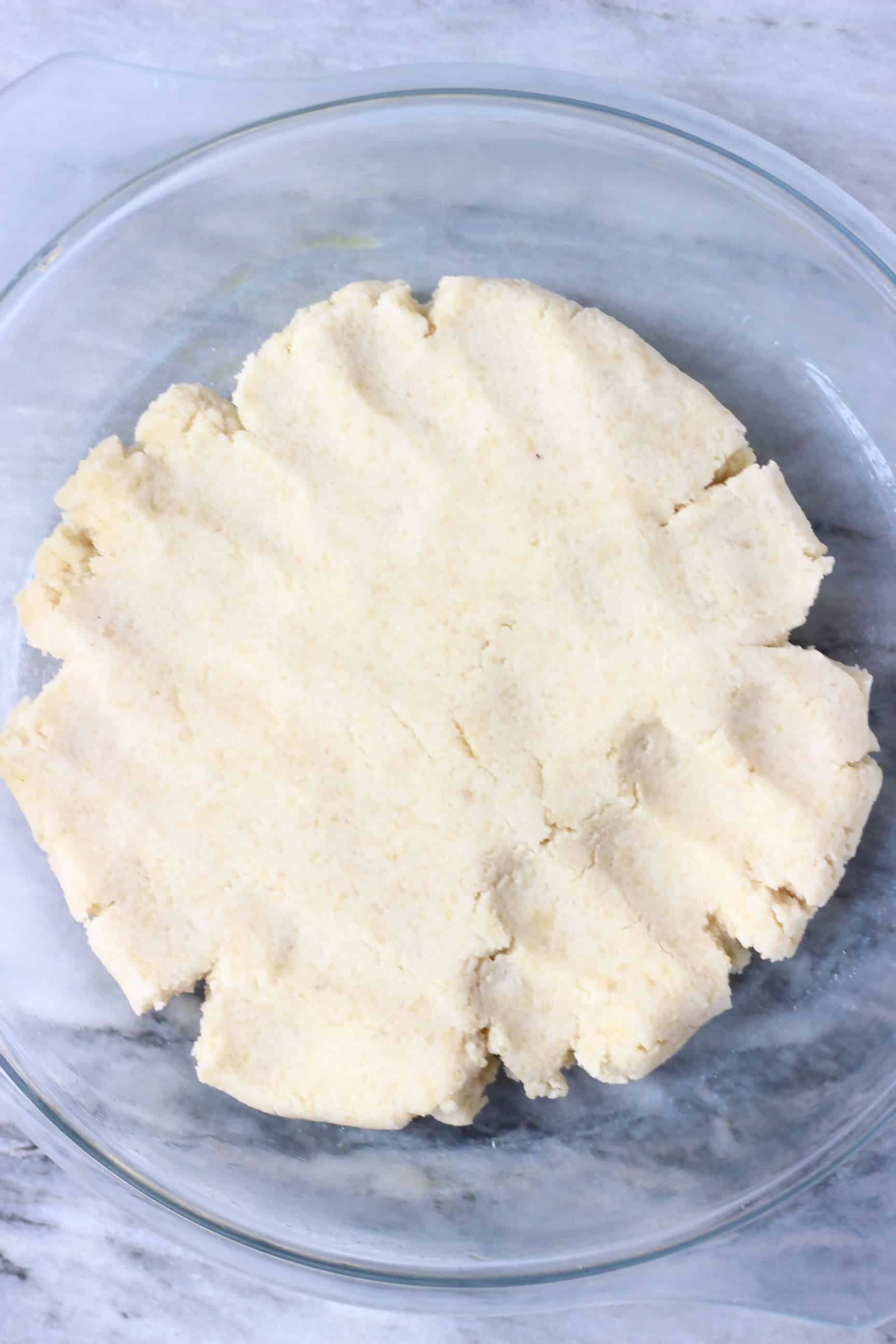 Raw gluten-free vegan pastry dough being pressed into a glass pie dish