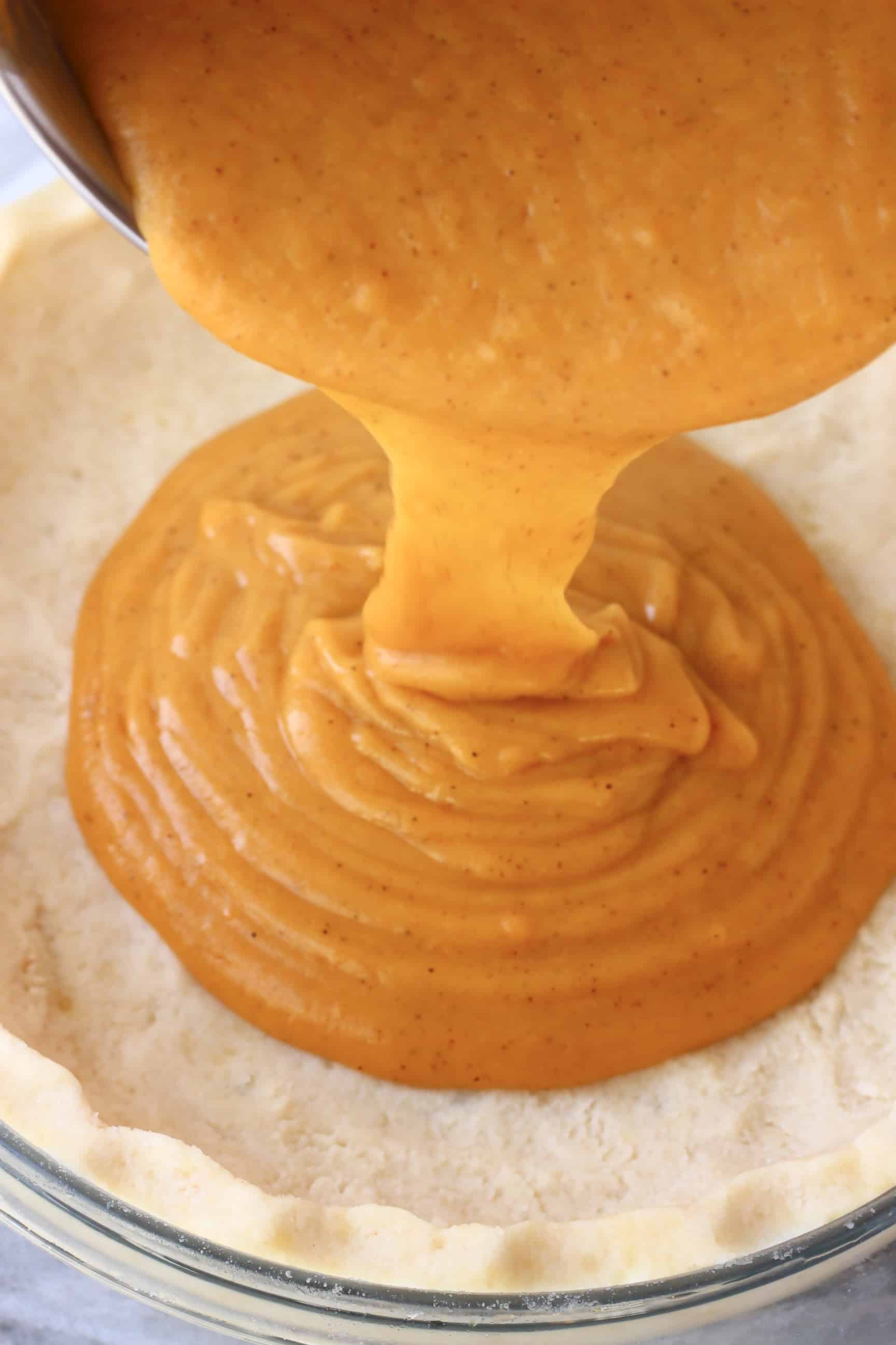 Orange vegan sweet potato pie filling being poured into a raw pastry crust in a pie dish