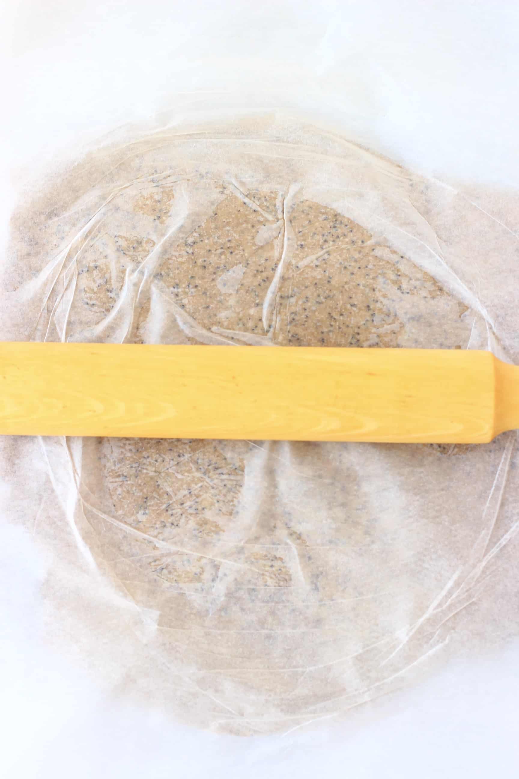 Raw gluten-free vegan crackers mixture between two sheets of baking paper being rolled out with a rolling pin