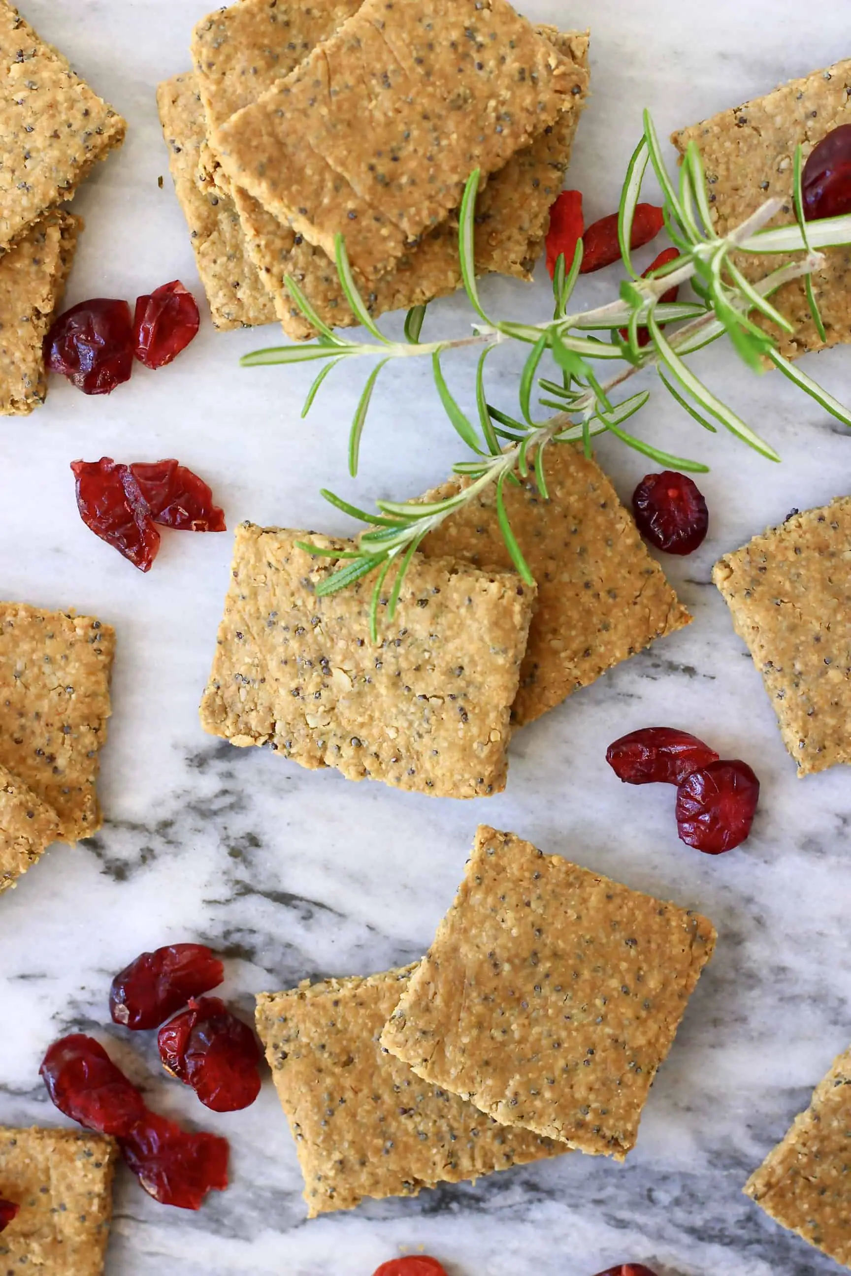 Several square gluten-free vegan crackers with dried cranberries and rosemary on a marble background