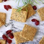 Several square gluten-free vegan crackers with dried cranberries and rosemary