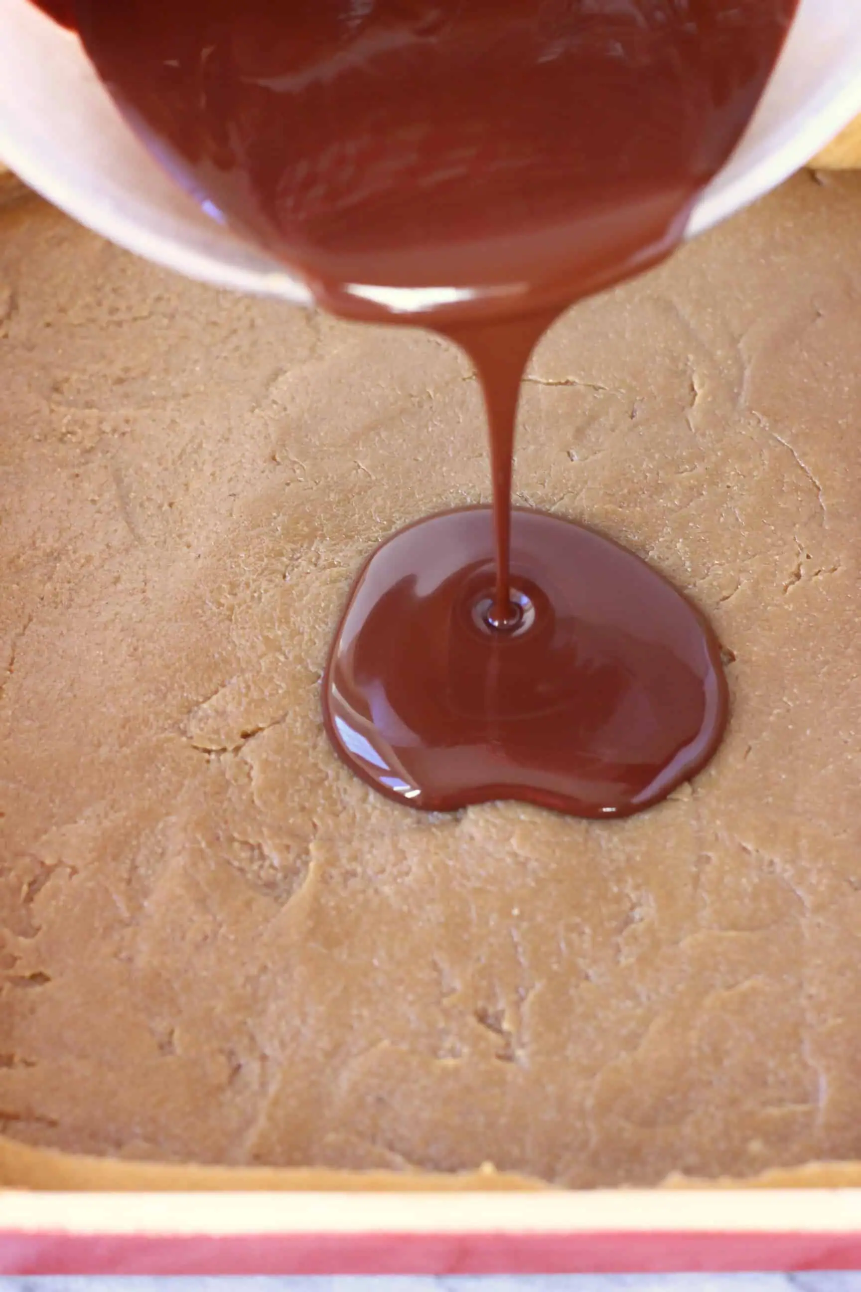 Melted chocolate being poured over a layer of vegan caramel