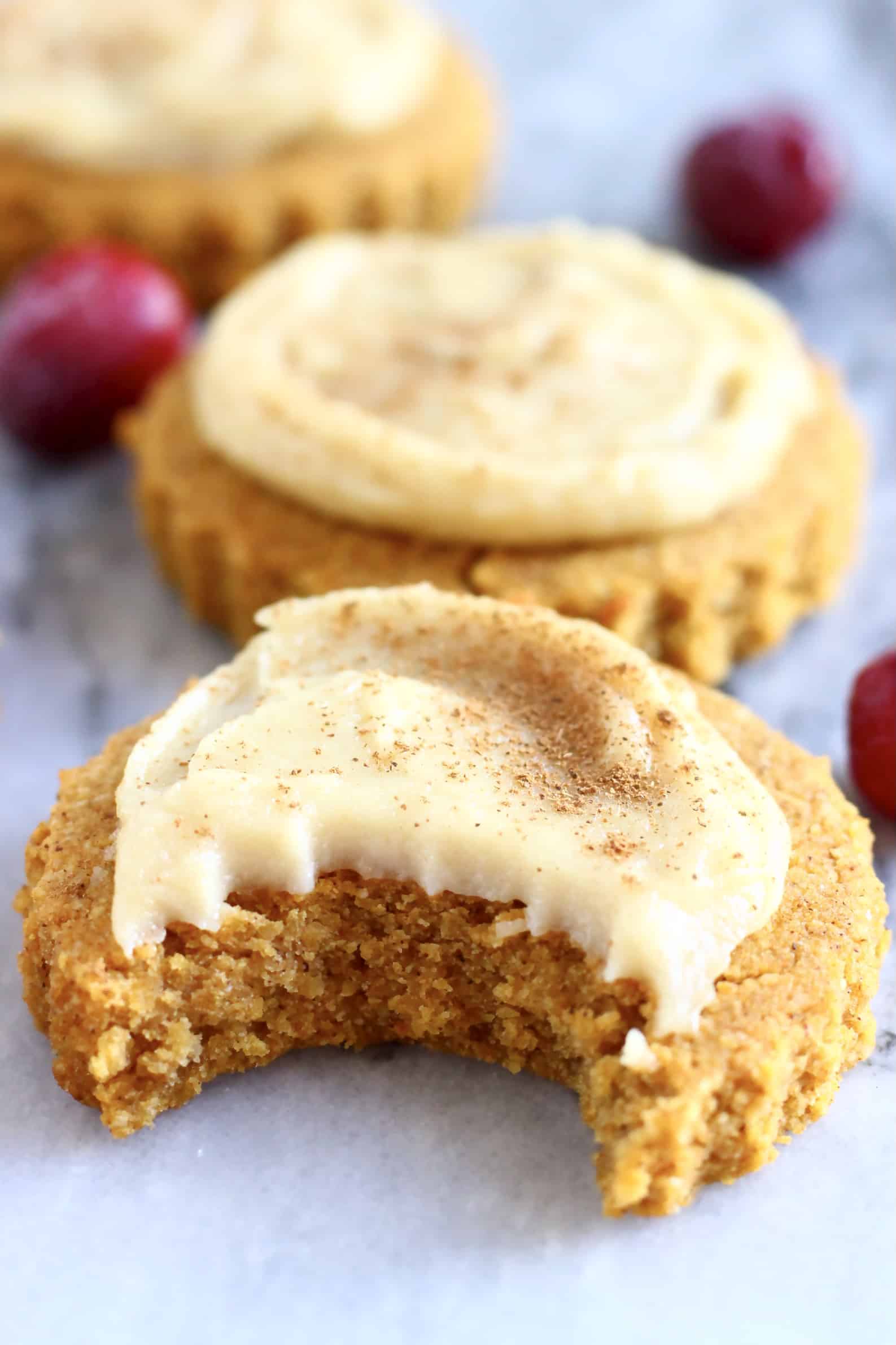 Two gluten-free vegan pumpkin sugar cookies topped with white frosting one with a bite taken out