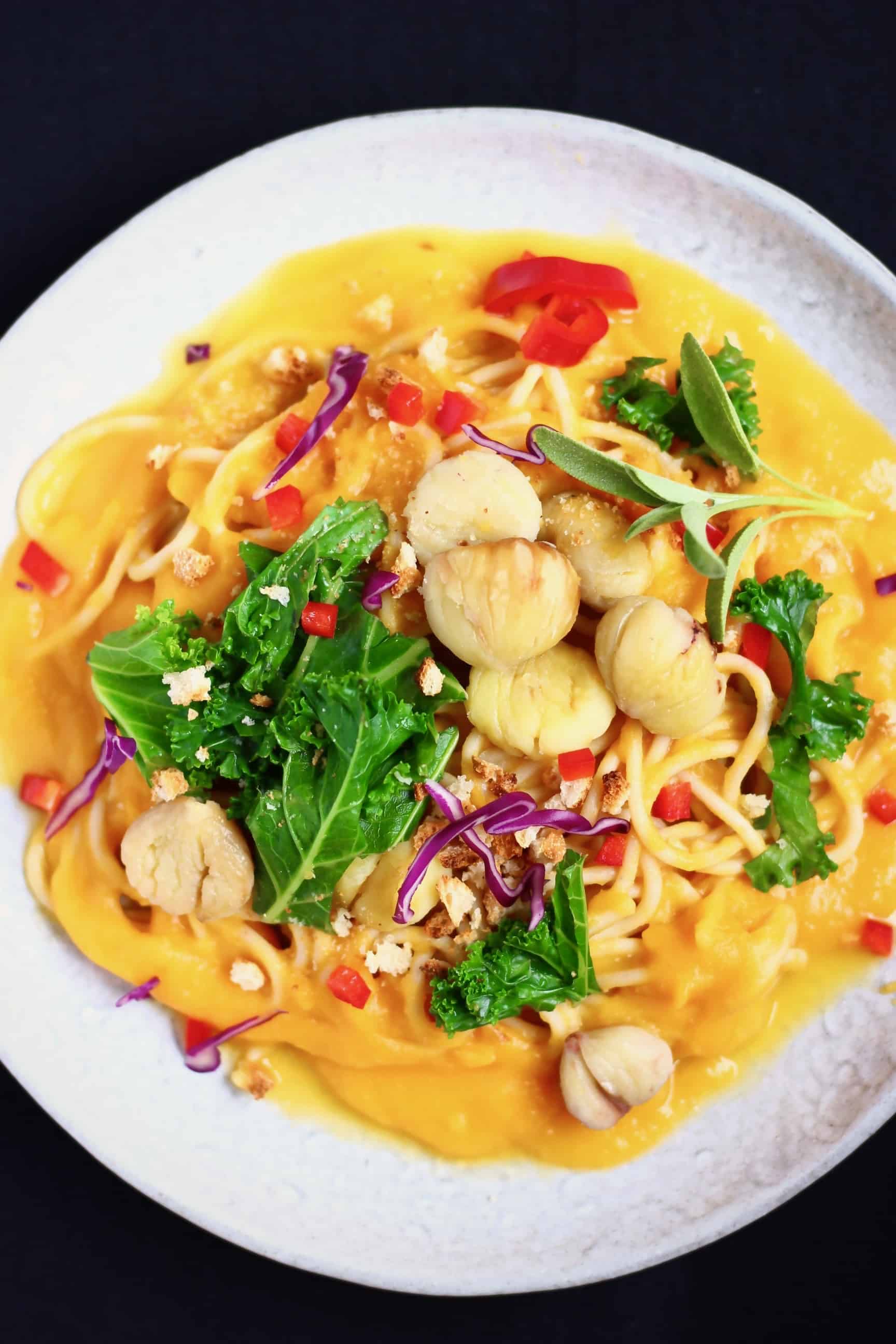 Spaghetti in an orange sauce topped with chestnuts and kale on a grey plate against a black background