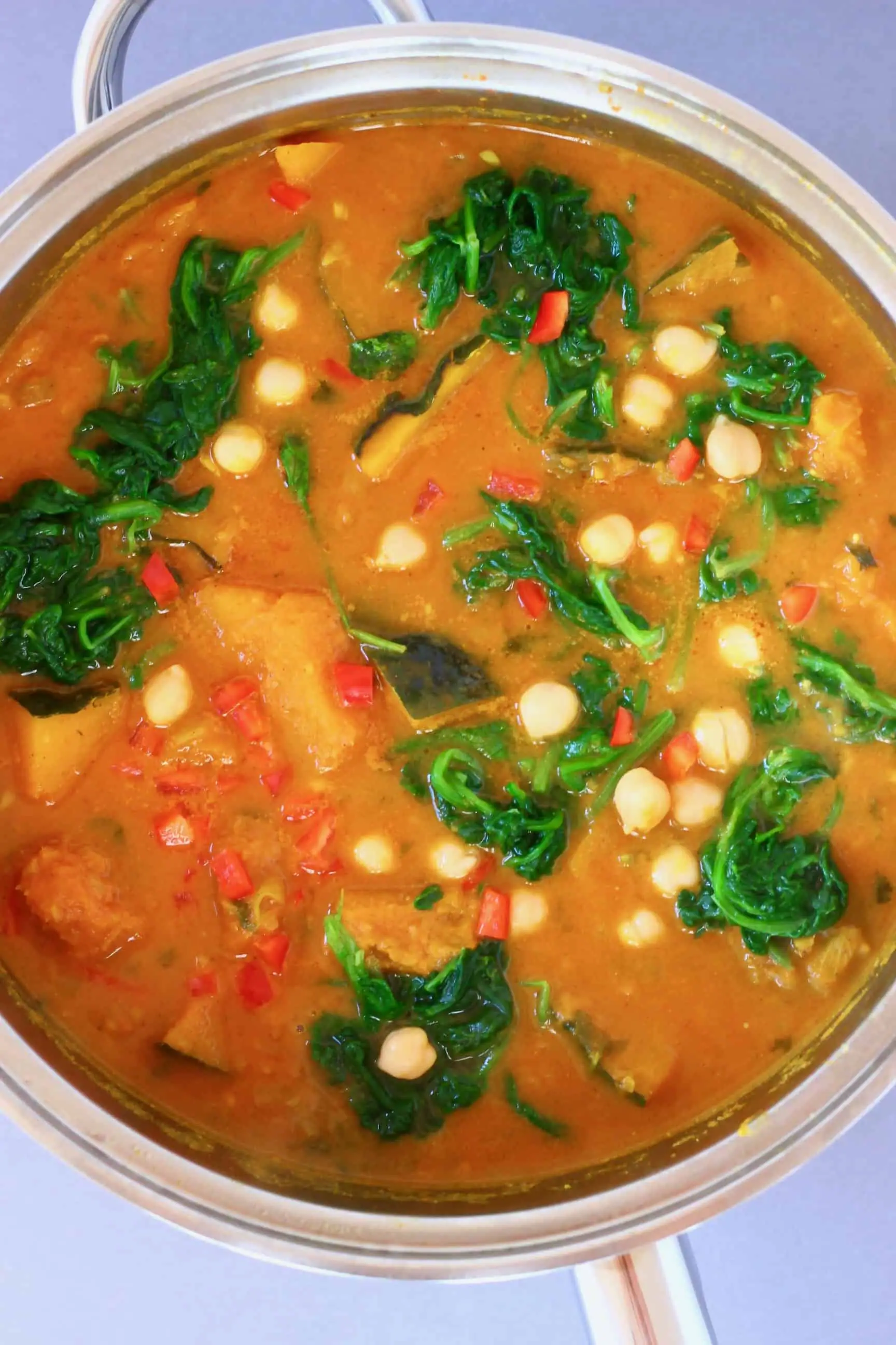 Diced pumpkin, chickpeas and spinach in a yellow curry sauce in a silver saucepan