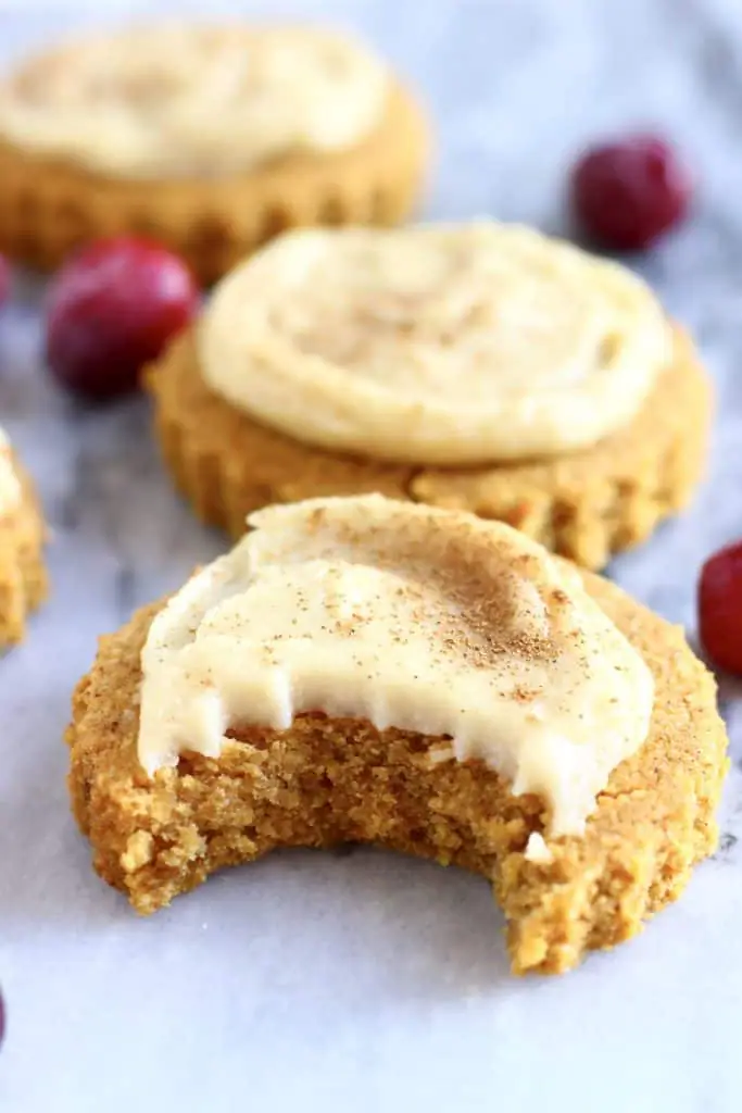 Two gluten-free vegan pumpkin sugar cookies topped with white frosting one with a bite taken out