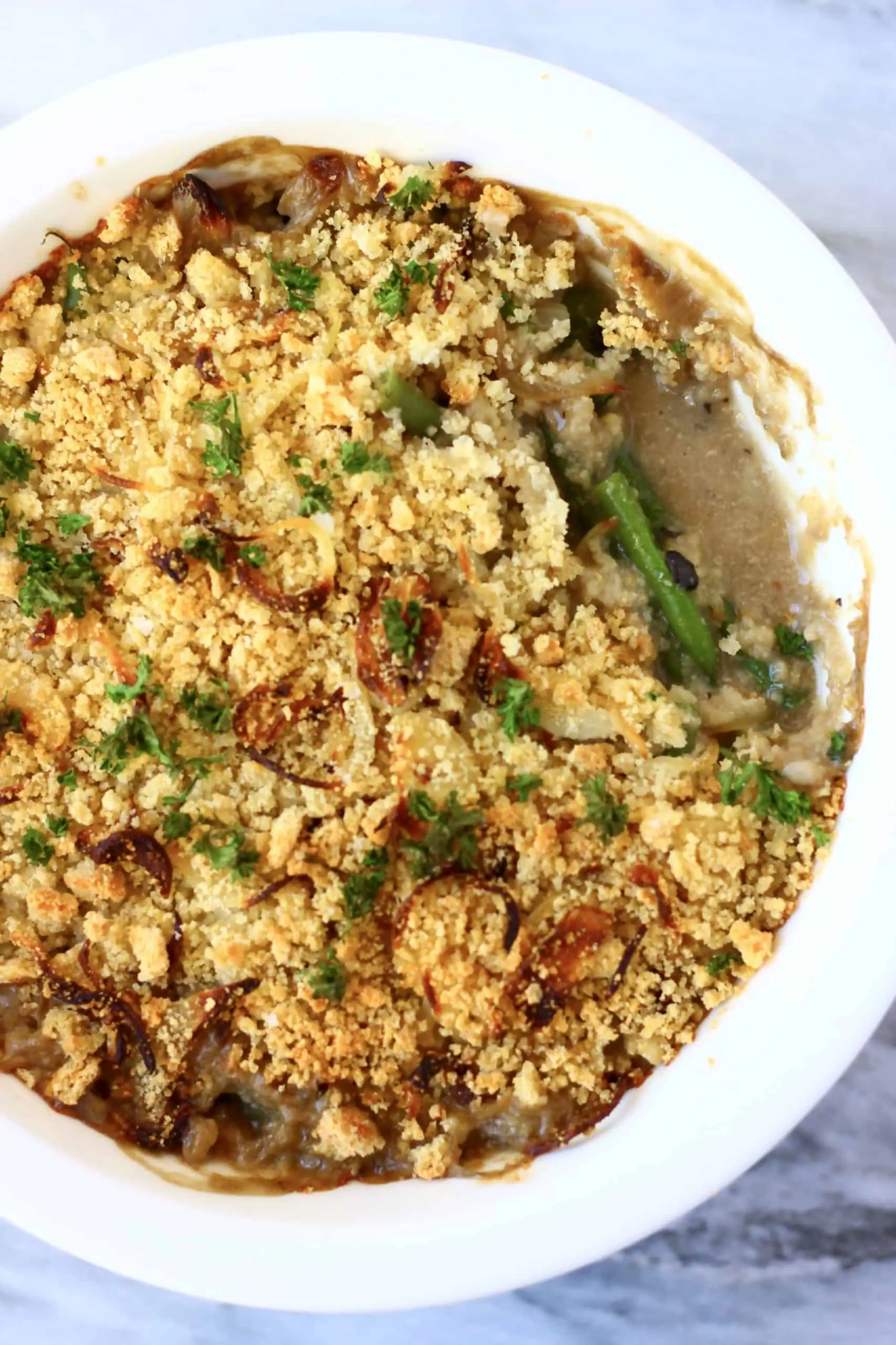 Green bean casserole topped with breadcrumbs and parsley in a white pie dish with a mouthful taken out