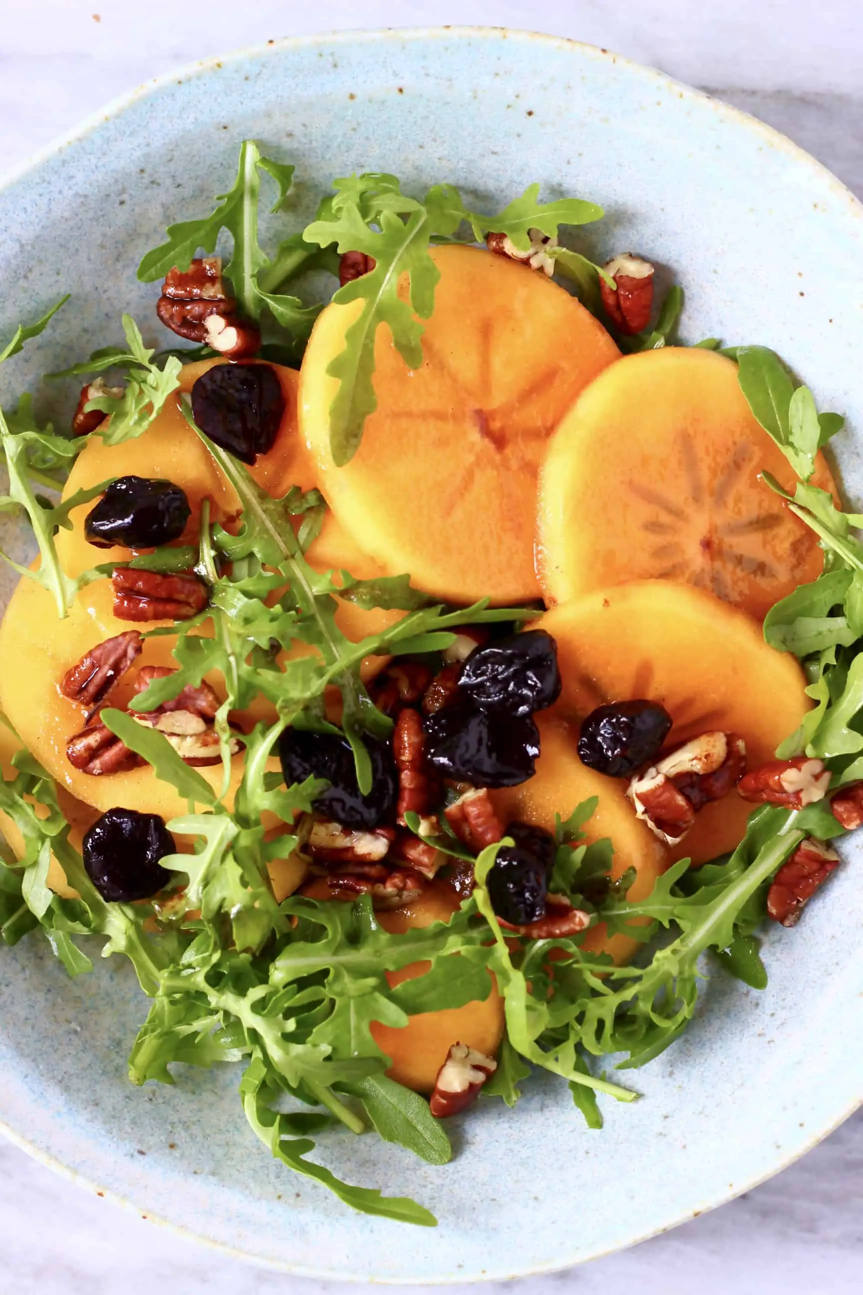 Persimmon salad in a blue bowl against a marble background