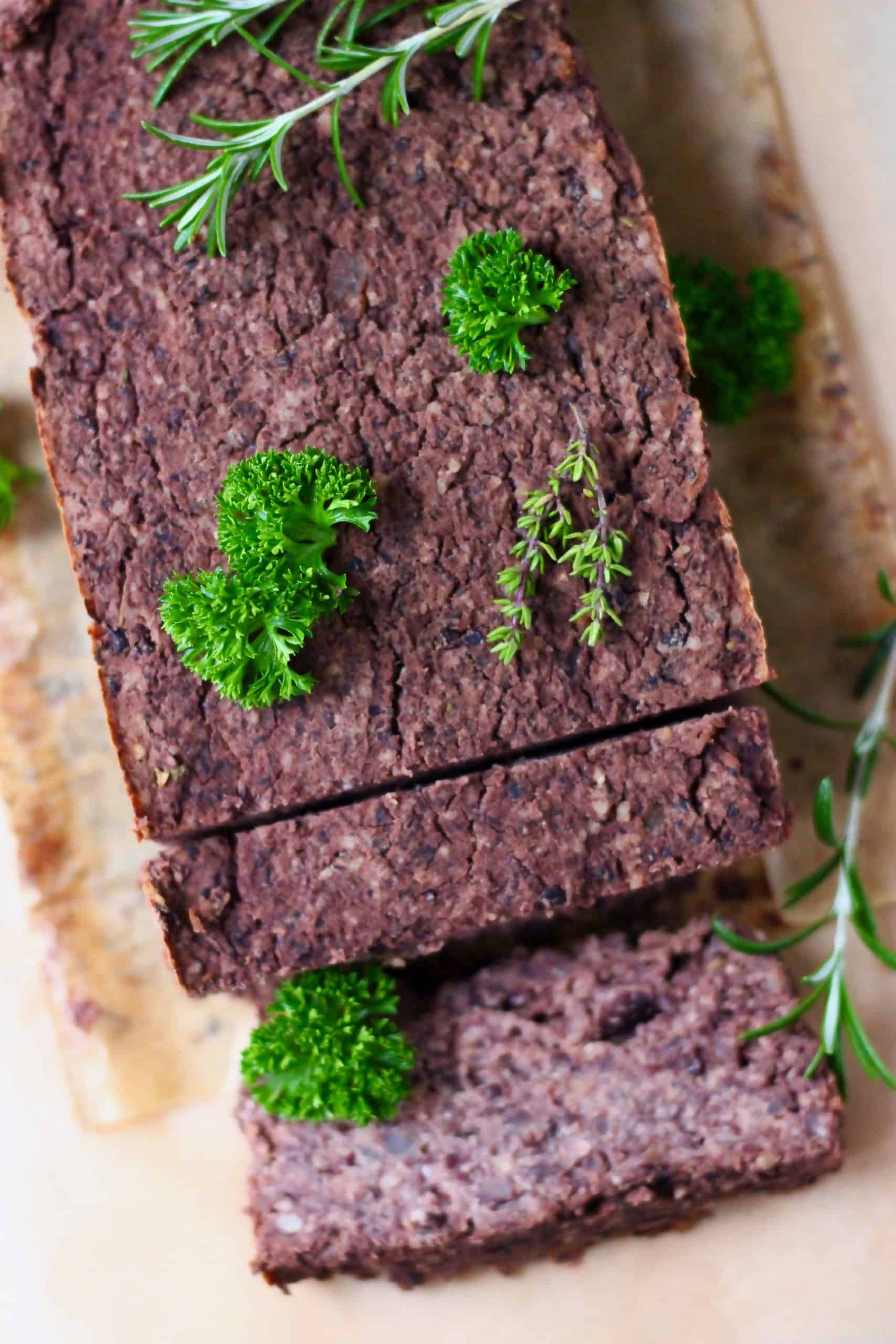 Un pastel de carne negro con dos rebanadas tomadas sobre papel de hornear marrón, espolvoreado con hierbas verdes frescas