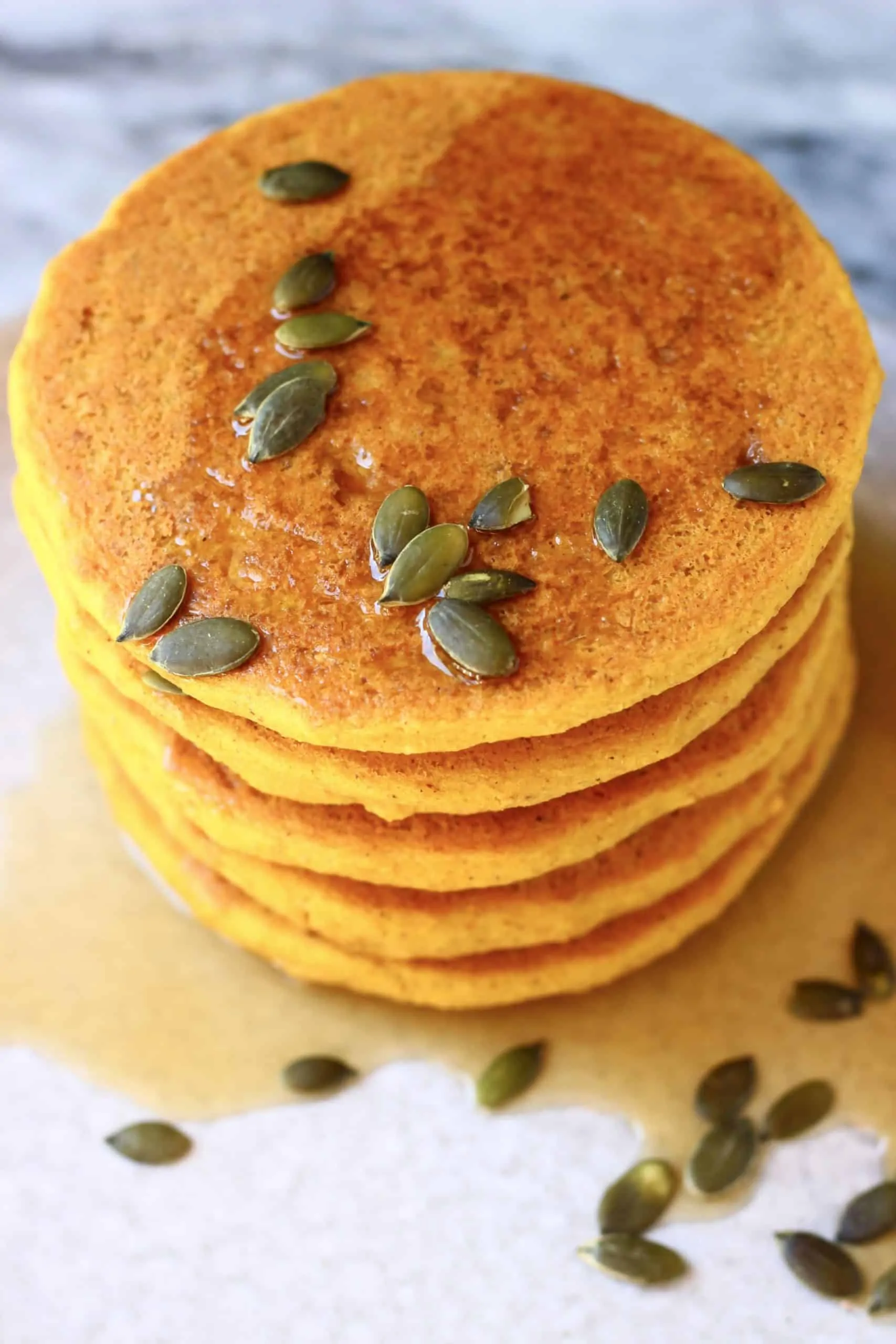 A stack of gluten-free vegan pancakes on a plate topped with syrup and pumpkin seeds