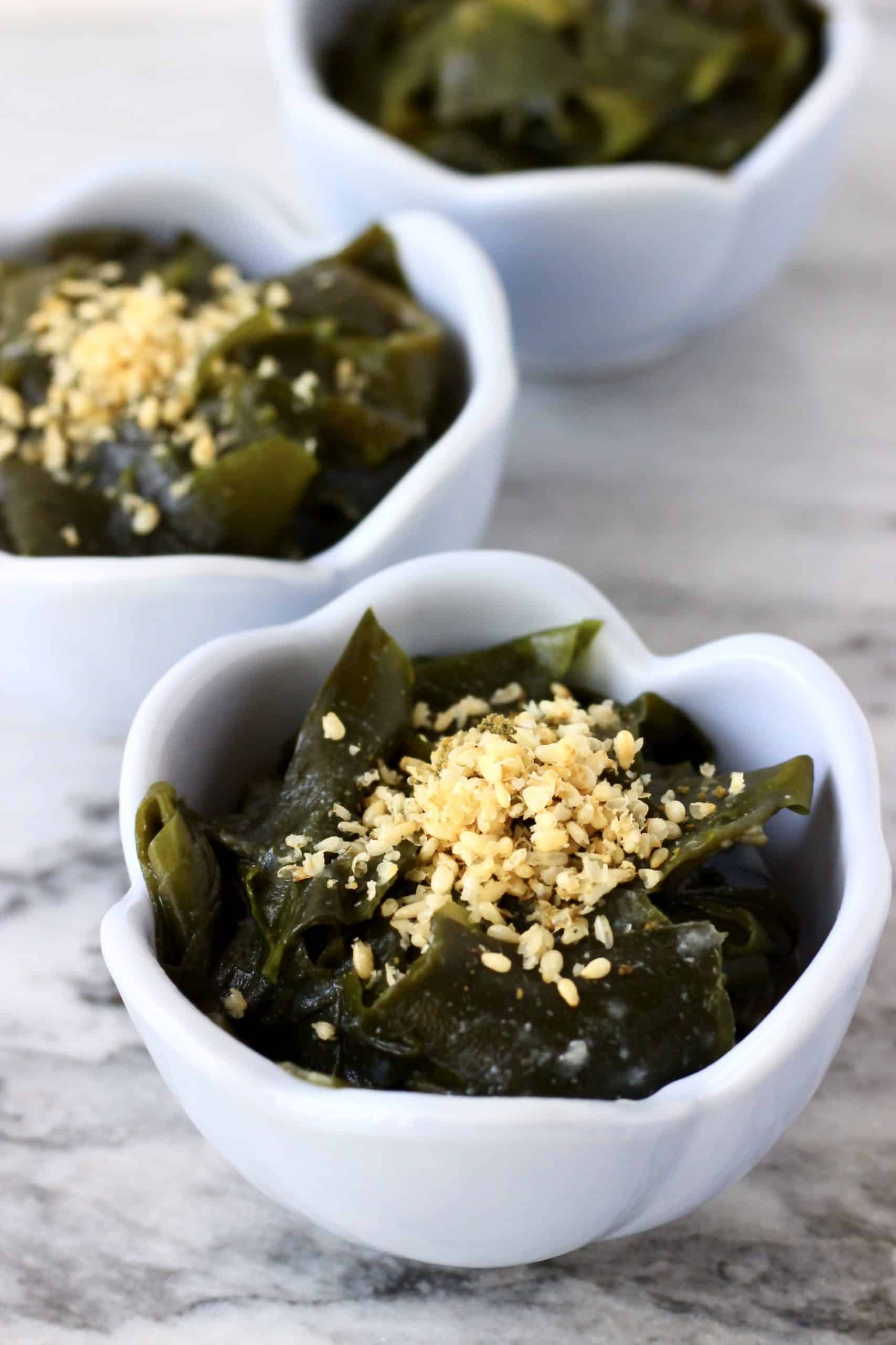 Seaweed salad topped with sesame seeds in three small blue bowls 