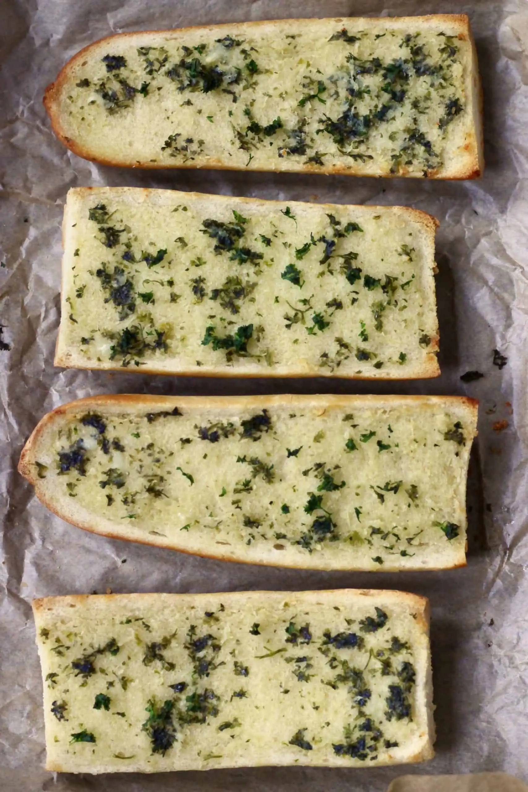 Four pieces of garlic bread on a sheet of brown baking paper