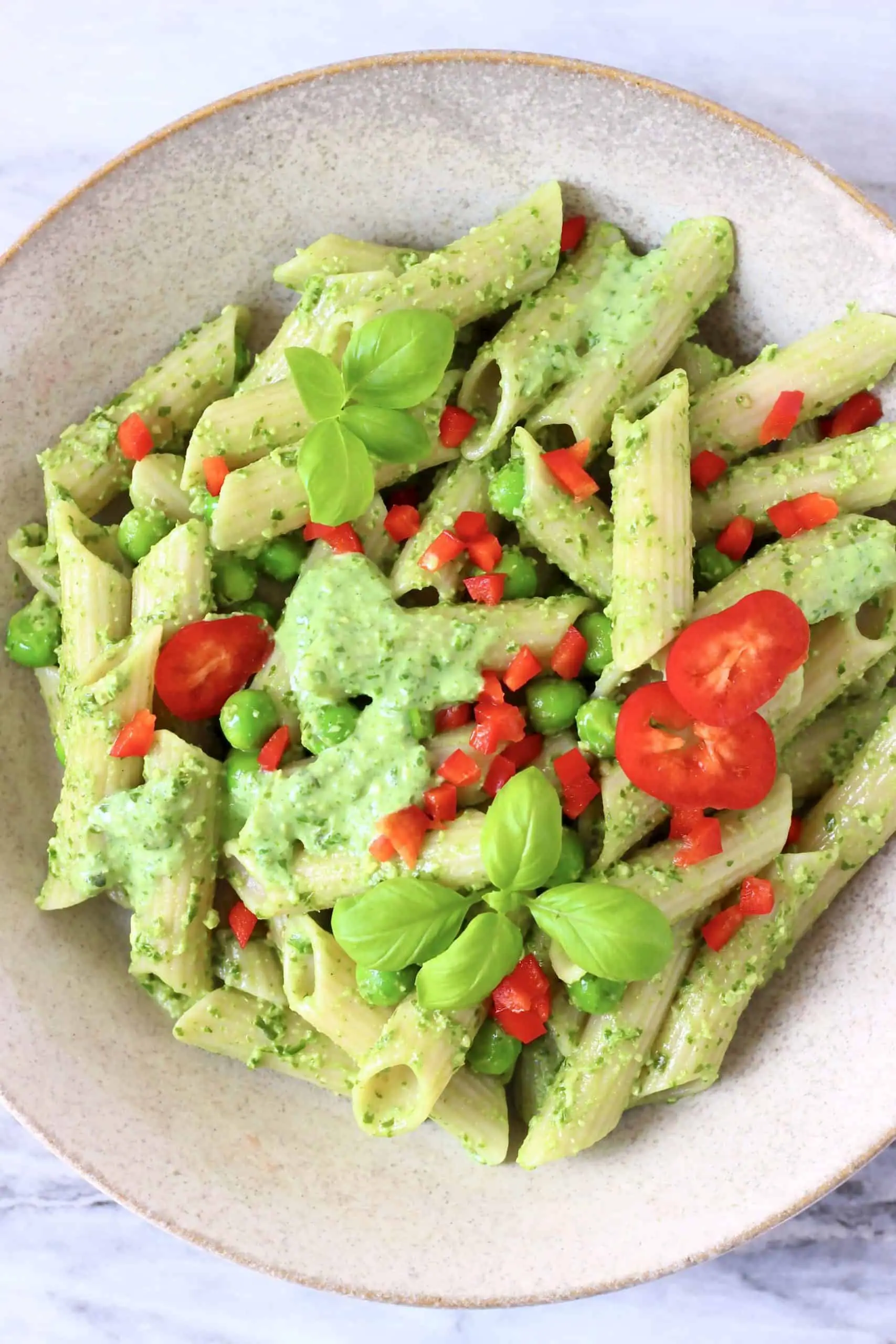 Penne pasta with pesto sauce, green peas and chopped red pepper in a beige bowl 
