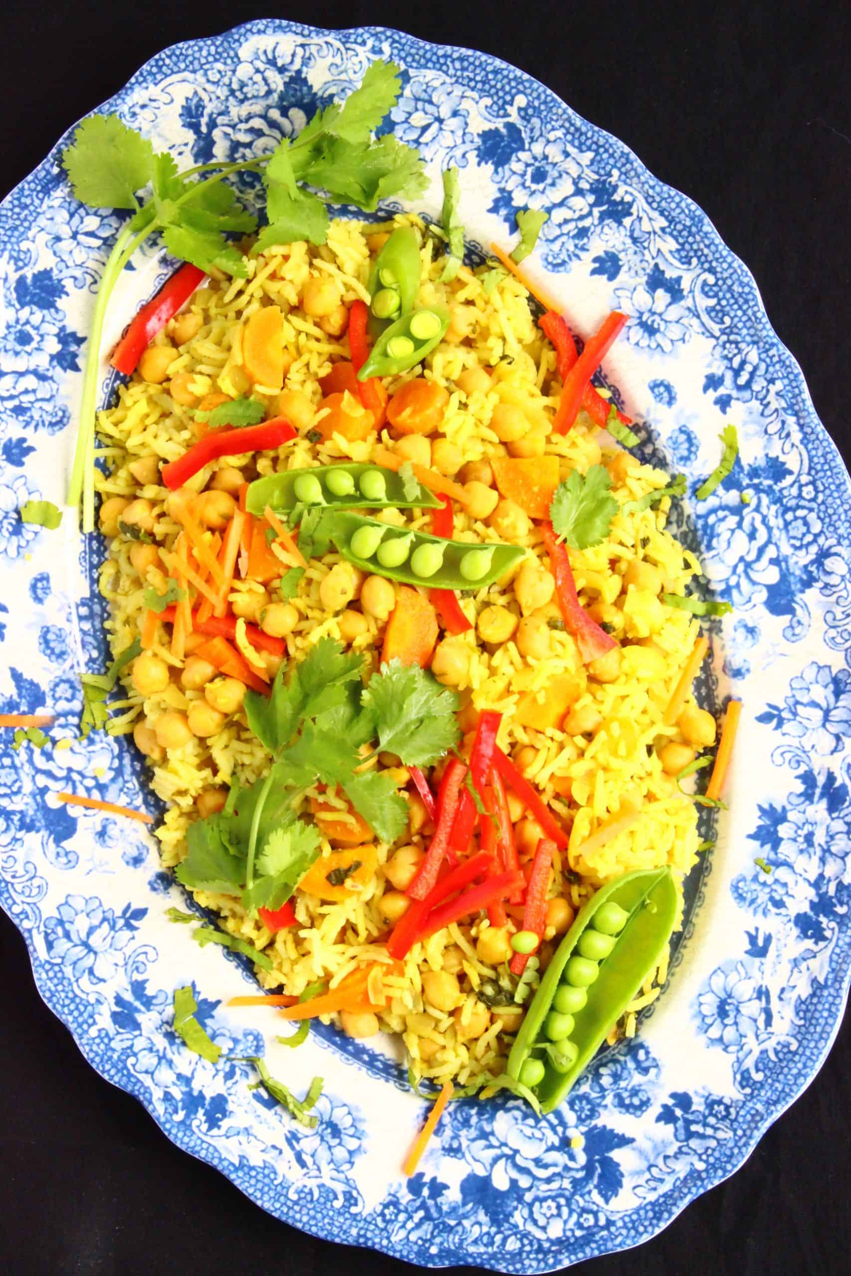 Yellow rice with green and red vegetables on a blue patterned plate 