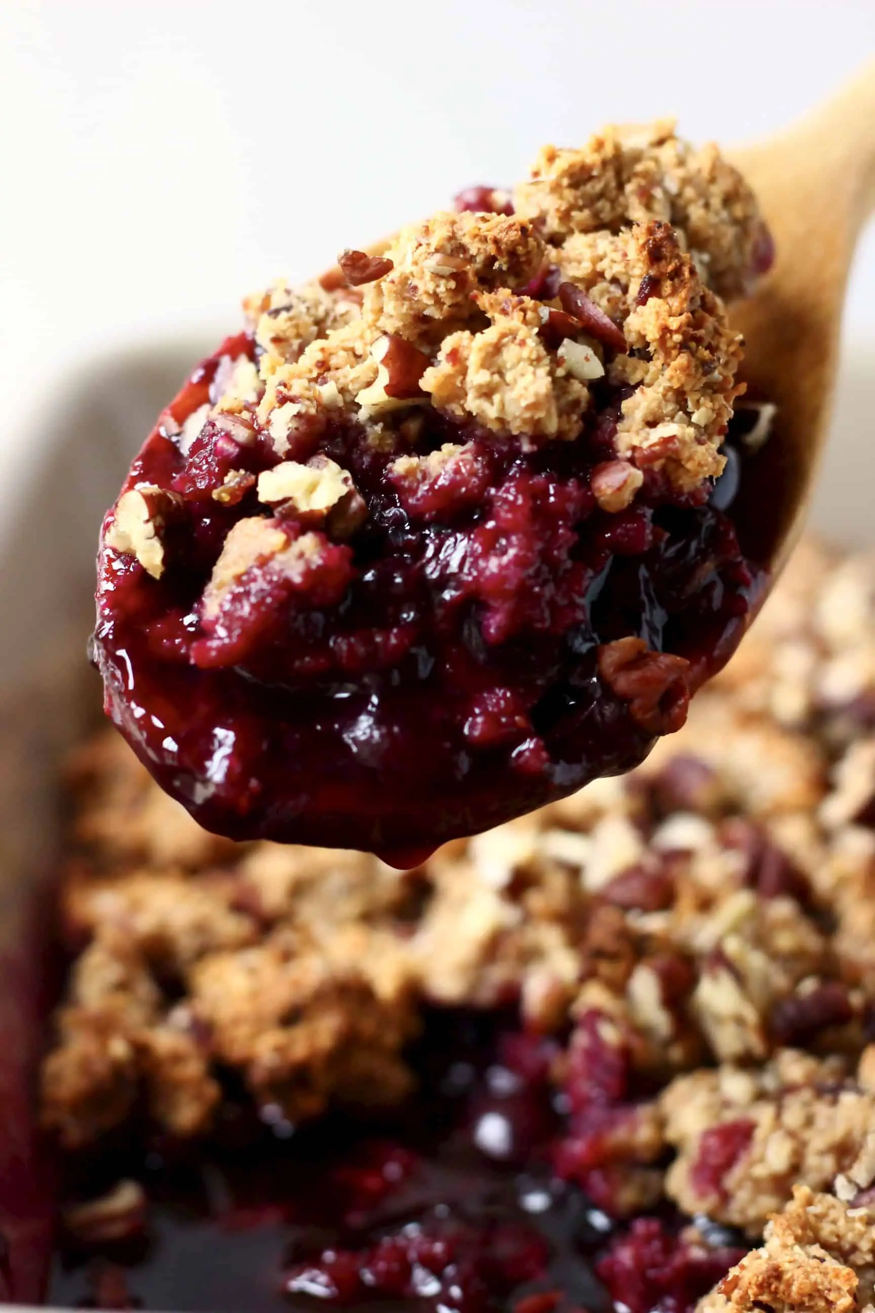 A grey rectangular baking dish of blueberry crisp with a wooden spoon lifting up a mouthful 