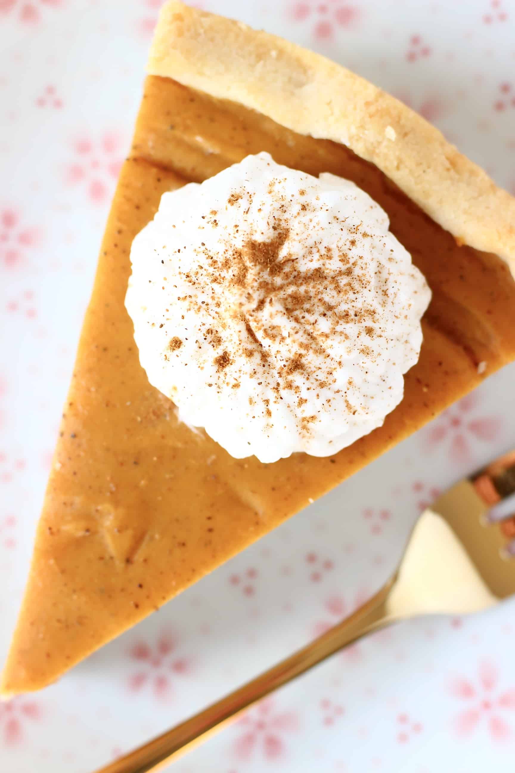 A slice of sweet potato pie topped with white cream on a plate with a gold fork