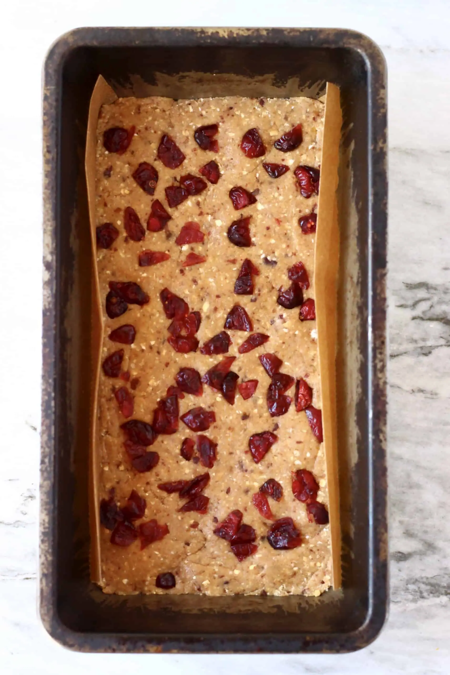 Vegan protein bar mixture topped with dried cranberries in a loaf tin lined with baking paper