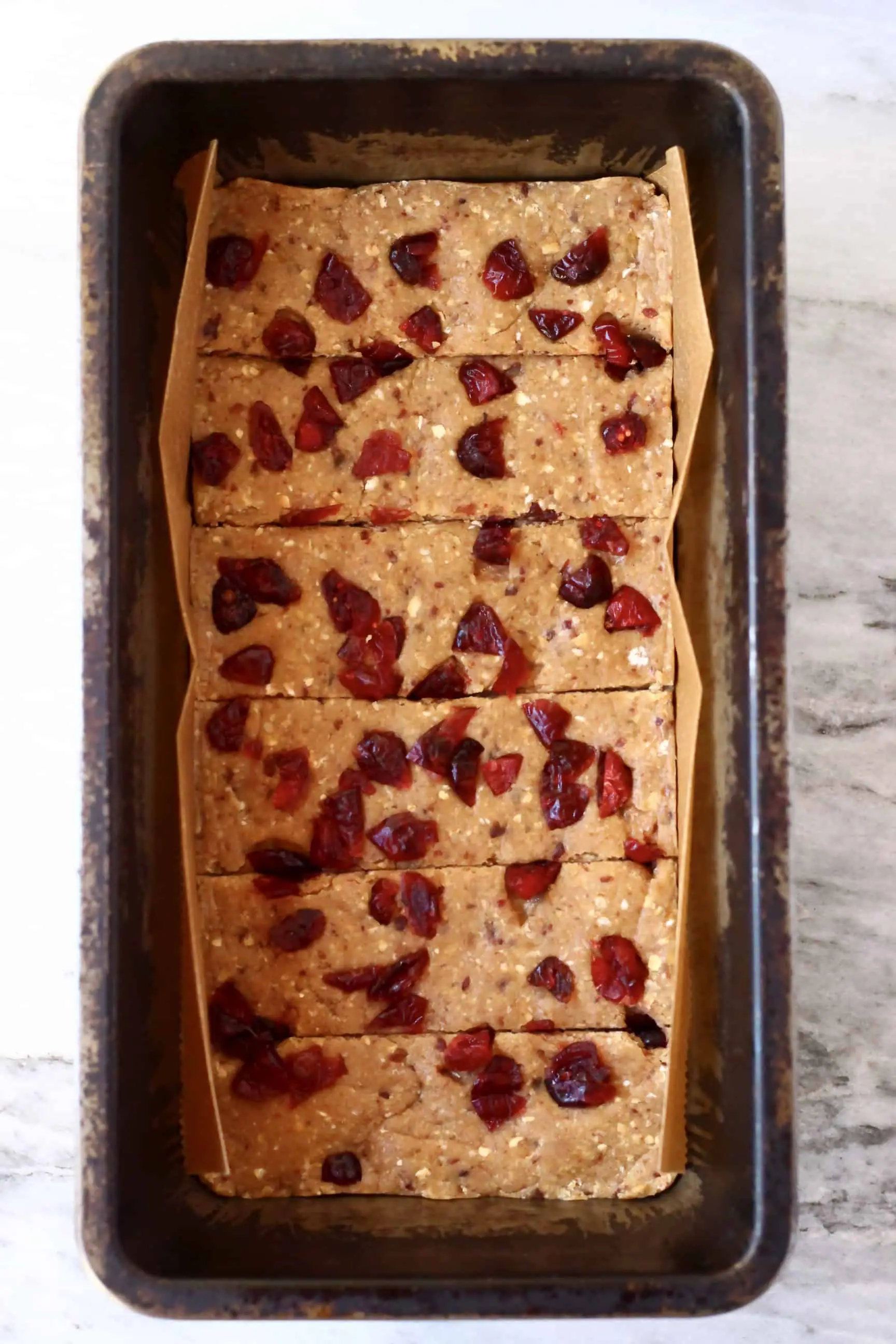 Vegan protein bar mixture topped with dried cranberries in a loaf tin cut into six bars