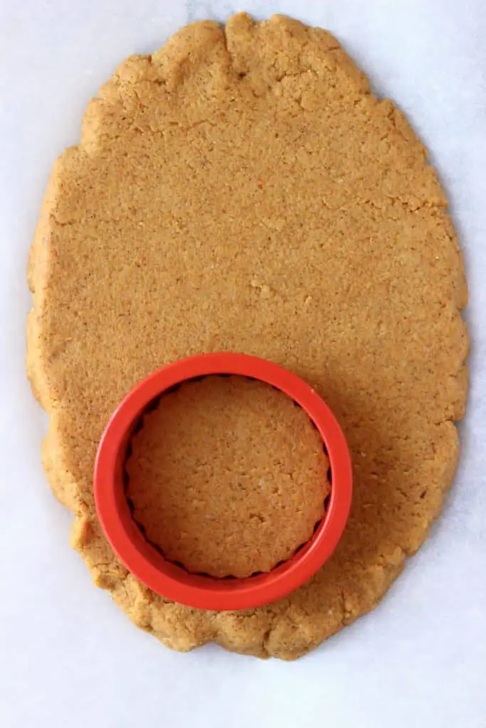 Raw gluten-free vegan pumpkin sugar cookie dough rolled out on a white baking sheet with a circular cookie cutter