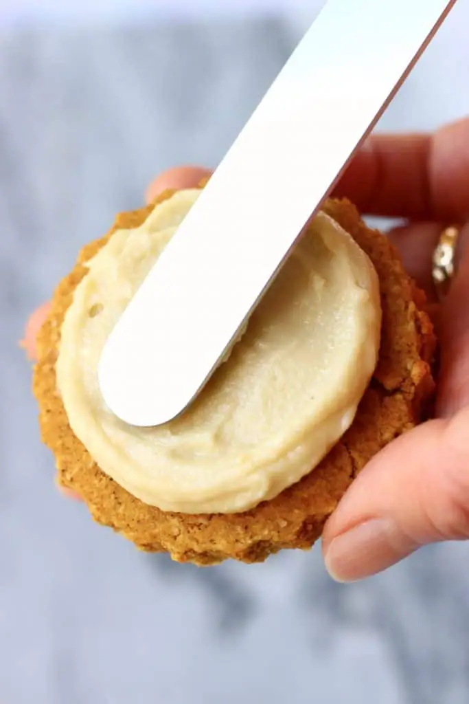 A knife spreading white frosting onto a pumpkin cookie