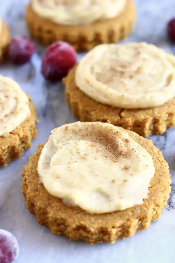 Four gluten-free vegan pumpkin sugar cookies topped with white frosting on a marble background