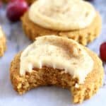 Two gluten-free vegan pumpkin sugar cookies topped with white frosting one with a bite taken out