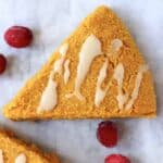 A triangular pumpkin scone drizzled with white icing on a marble background