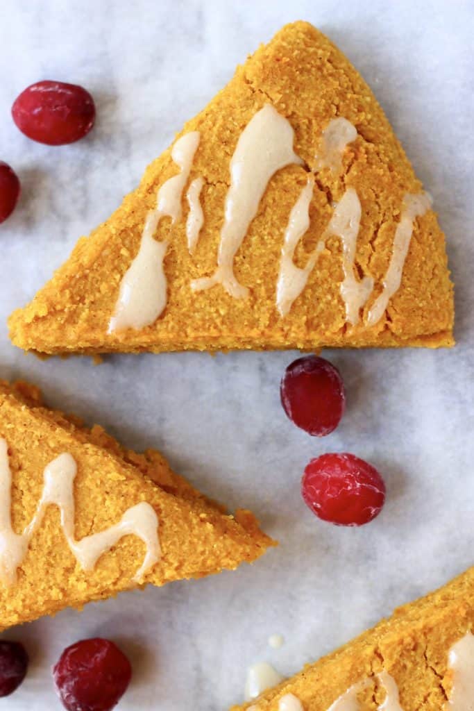 Three triangular pumpkin scones drizzled with white icing on a marble background