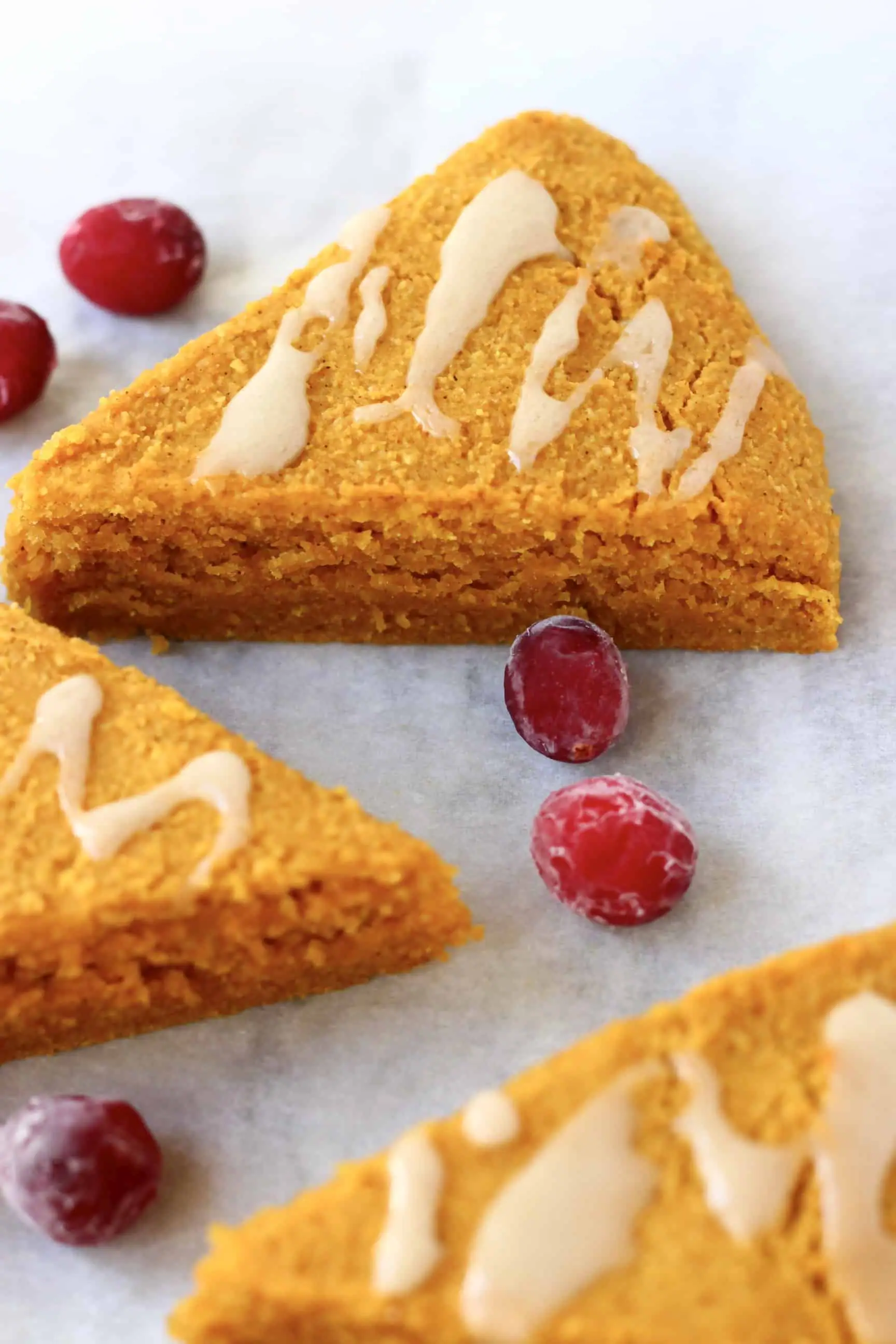 Three triangular pumpkin scones drizzled with white icing on a marble background