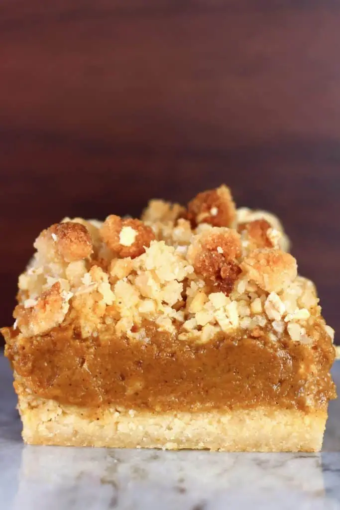 A vegan pumpkin pie bar with crumble topping against a brown background