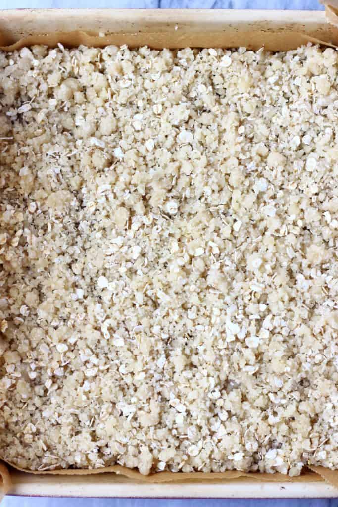 Crumble and oats on top of pumpkin pie filling in a square baking tin