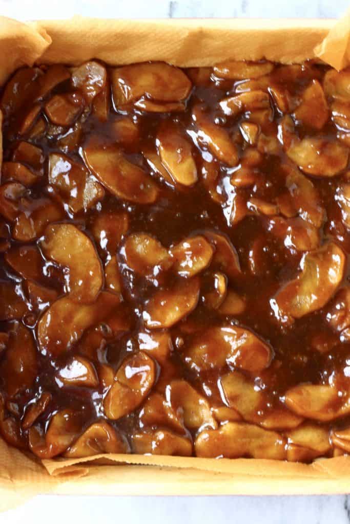 Cooked caramel sliced apples in a square baking tin over pastry