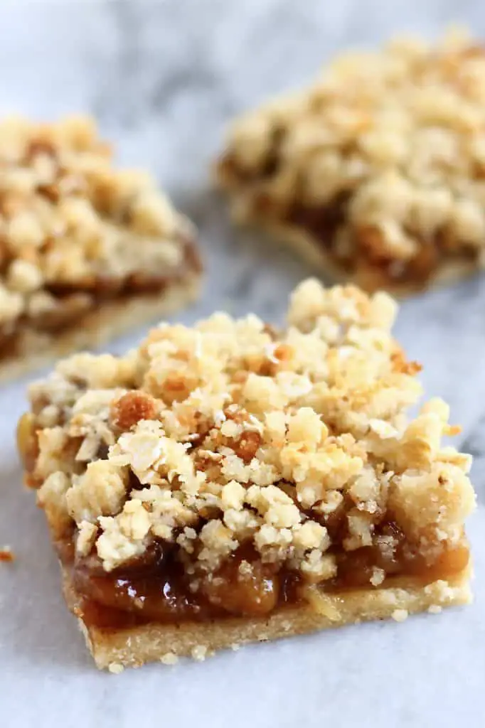 Three apple pie bars with crumble topping on a marble background
