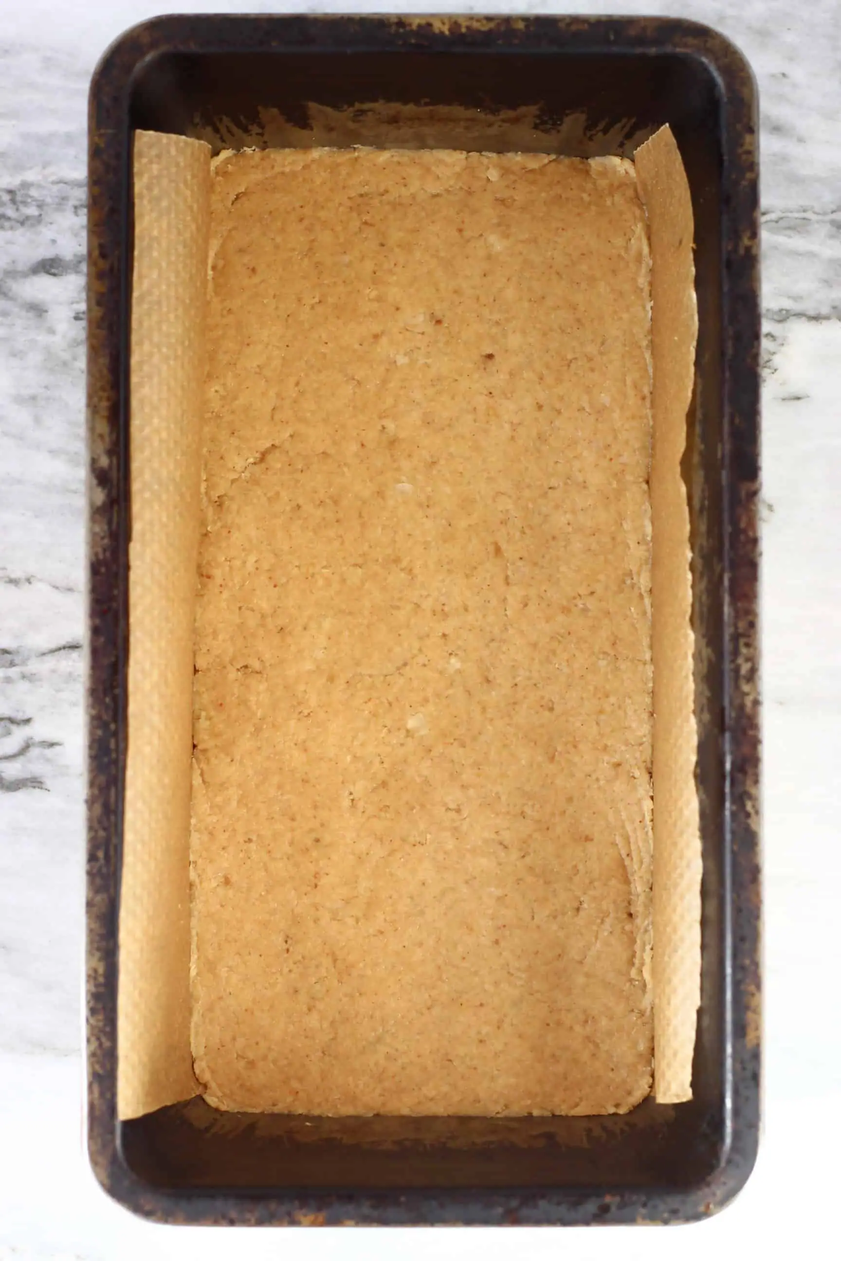 Peanut butter bar mixture in a loaf tin lined with baking paper