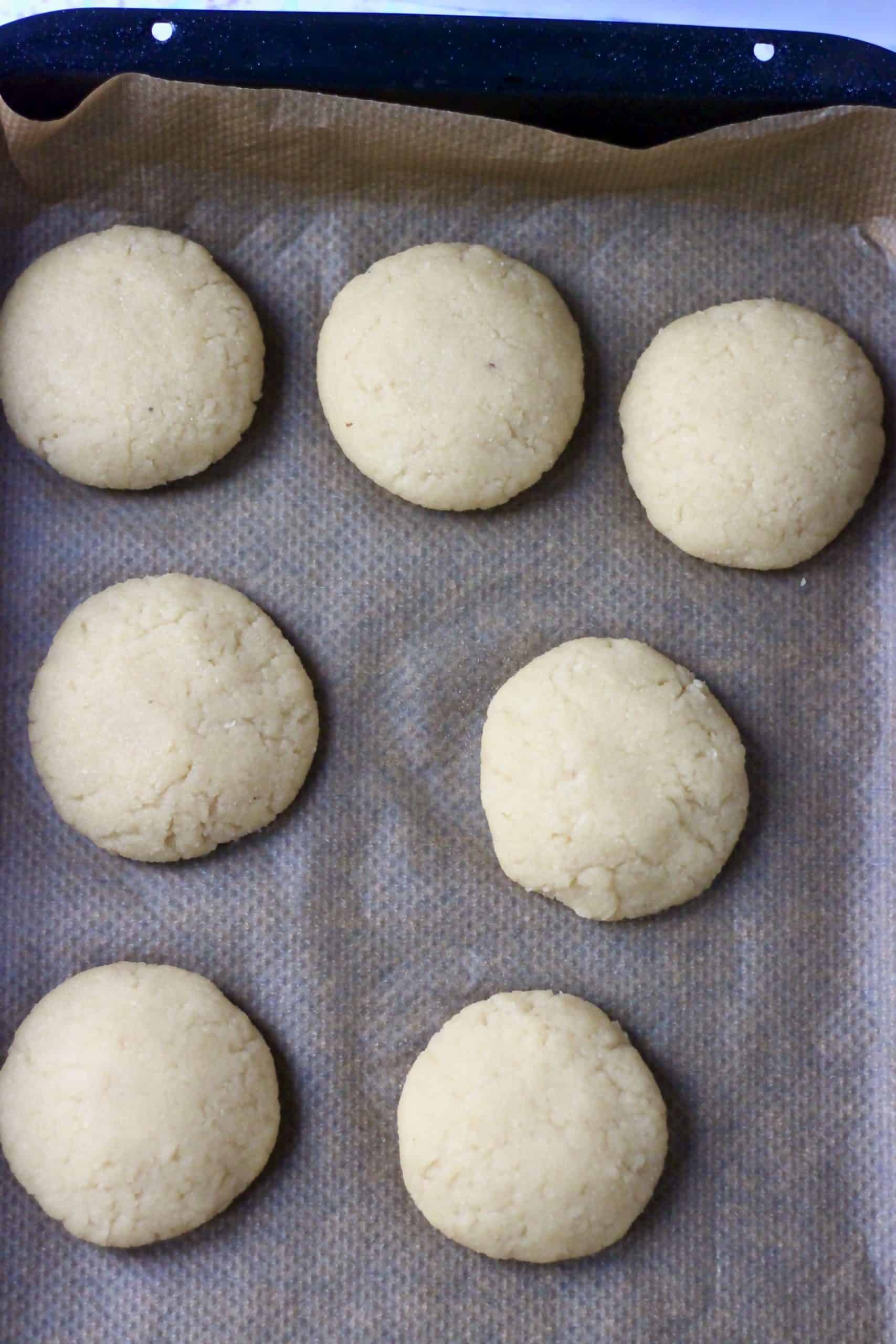 Seven raw gluten-free vegan lemon cookies on a baking tray lined with baking paper