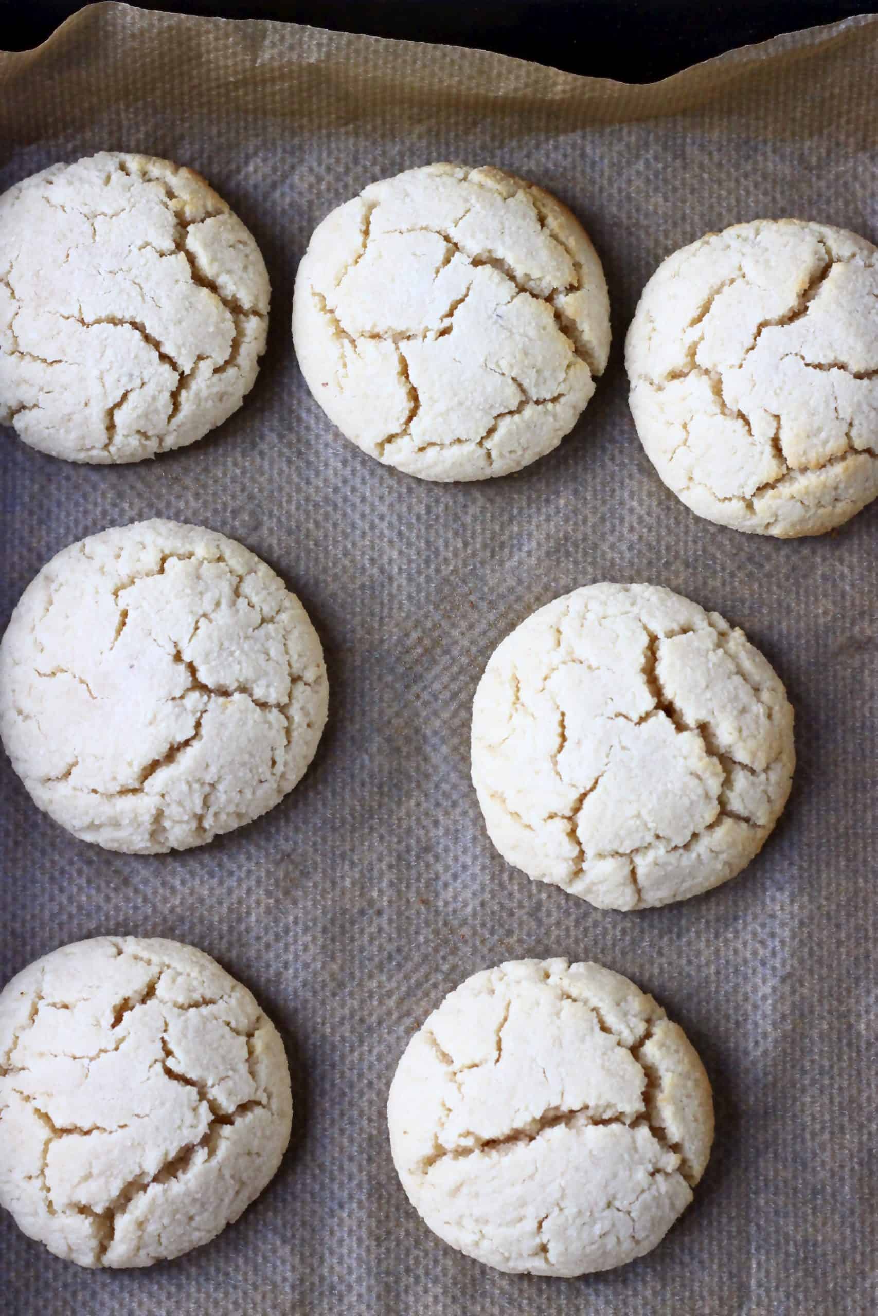 Seven gluten-free vegan lemon cookies on a baking tray lined with baking paper
