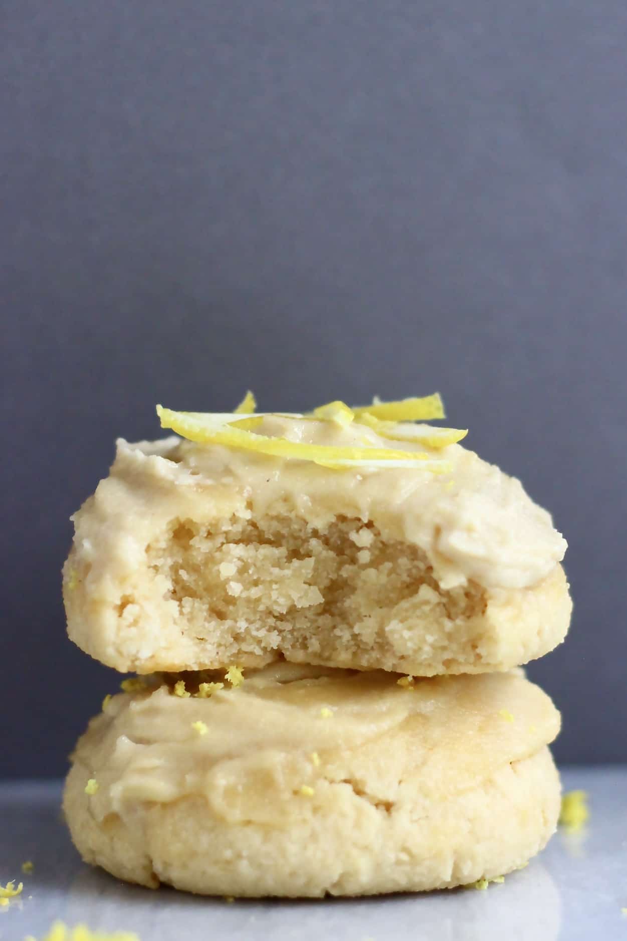 Two frosted gluten-free vegan lemon cookies, one with a bite taken out of it