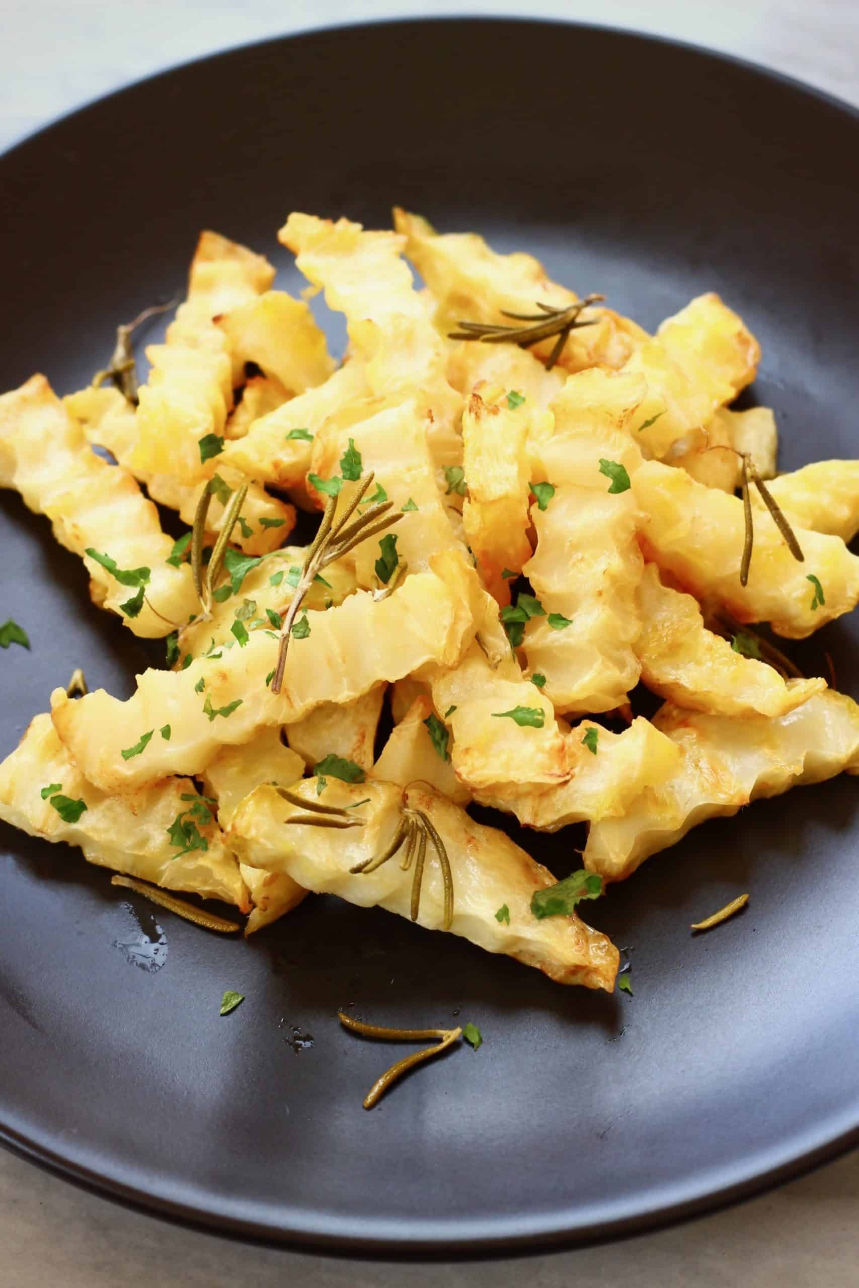 Crinkle-cut celeriac fries decorated with green herbs on a black plate